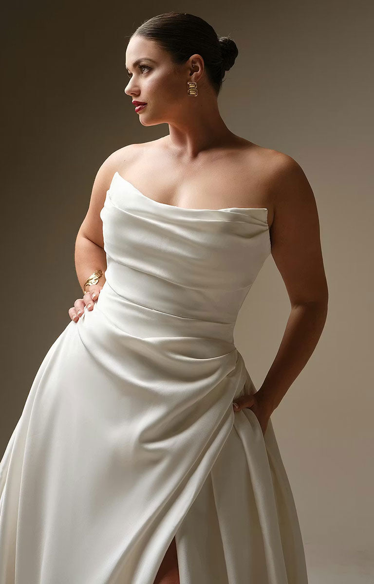 Woman wearing Kincaid by Sottero and Midgley - Ruched Satin Ballgown Wedding Dress with Pearl Details and Cat-Eye Neckline against a neutral background