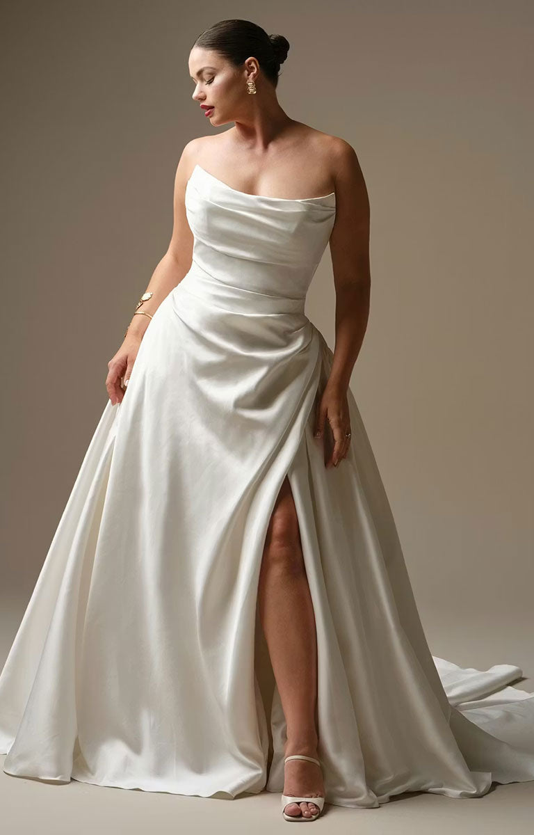 Woman wearing Kincaid by Sottero and Midgley - Ruched Satin Ballgown Wedding Dress with Pearl Details and Cat-Eye Neckline with a high slit on a plain background