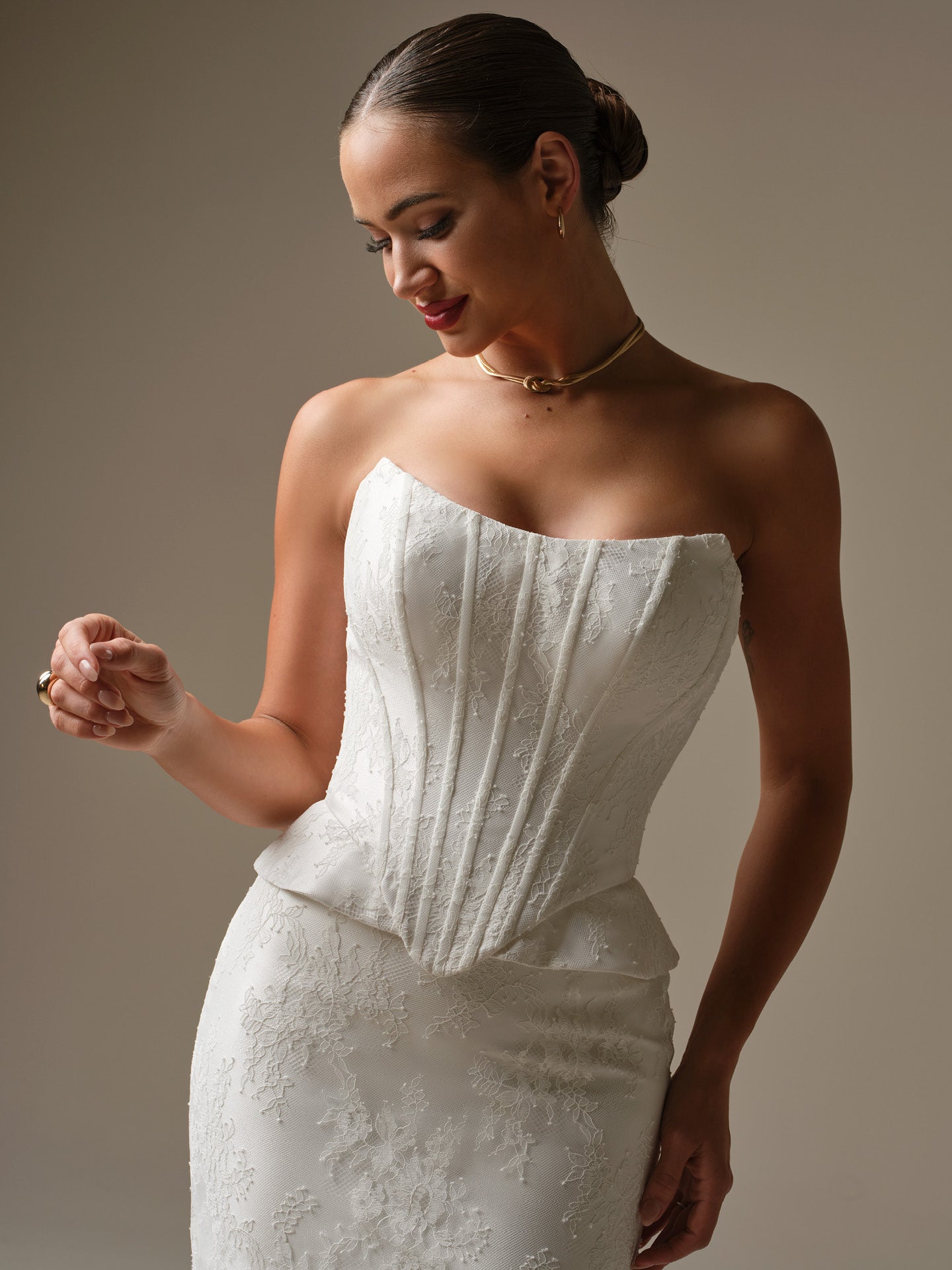 Woman wearing Lassen by Sottero and Midgley - Strapless Chantilly Lace Sheath Wedding Dress with Cat-Eye Neckline and Corset Bodice against a plain background