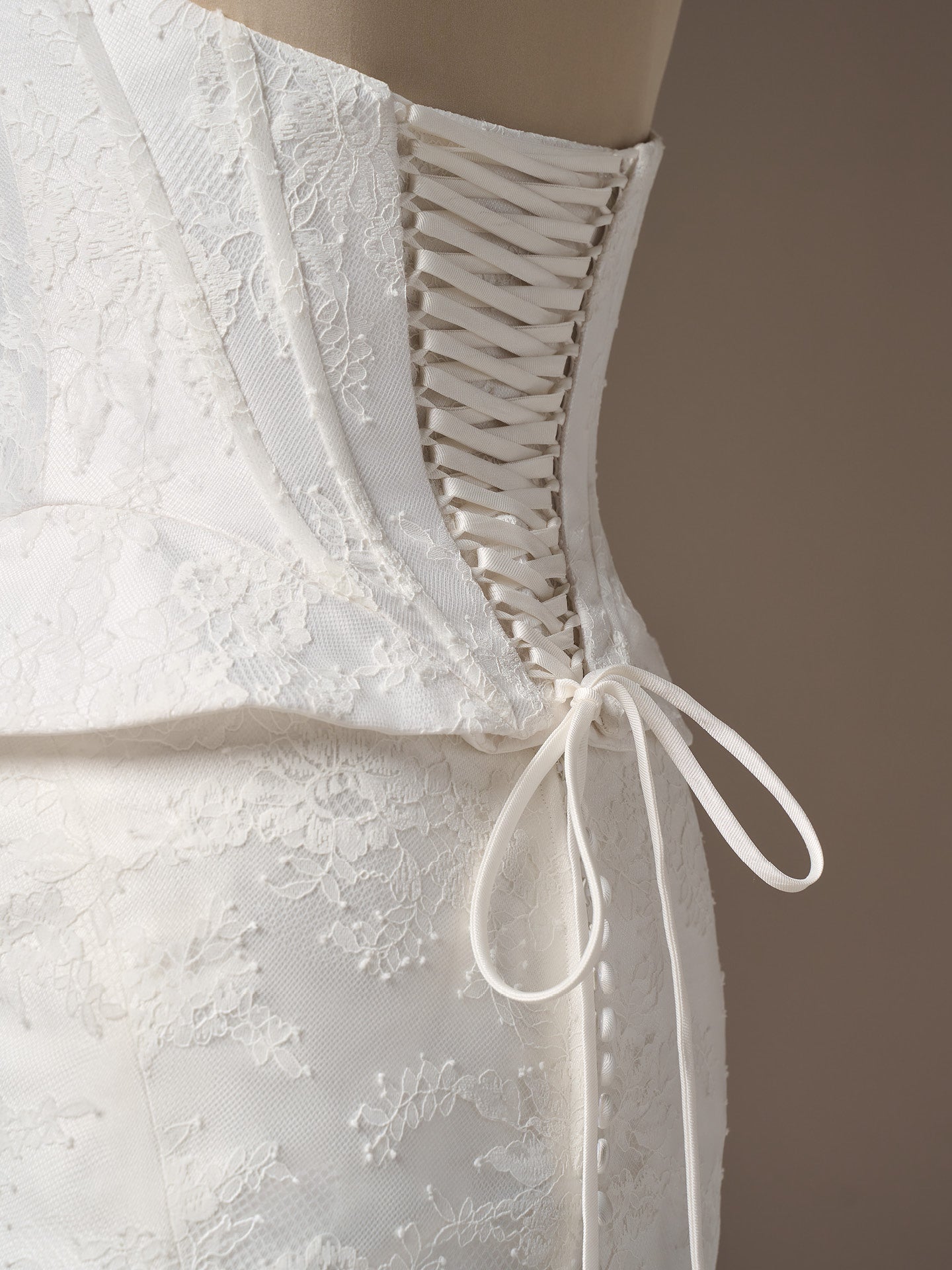 Close-up of Lassen by Sottero and Midgley - Strapless Chantilly Lace Sheath Wedding Dress with Cat-Eye Neckline  - showcasing the lace up corset bodice back with a brown background