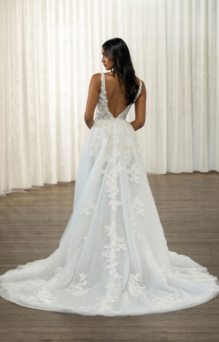 Woman wearing Tala by Madi Lane, a white wedding dress with floral details in a room with white curtains.