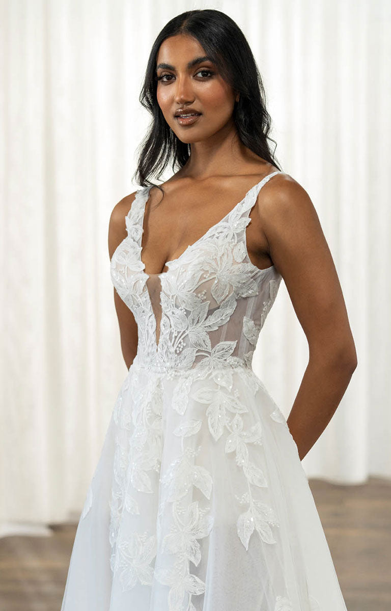 Woman wearing Tala by Madi Lane, a white lace wedding dress against a white curtain background