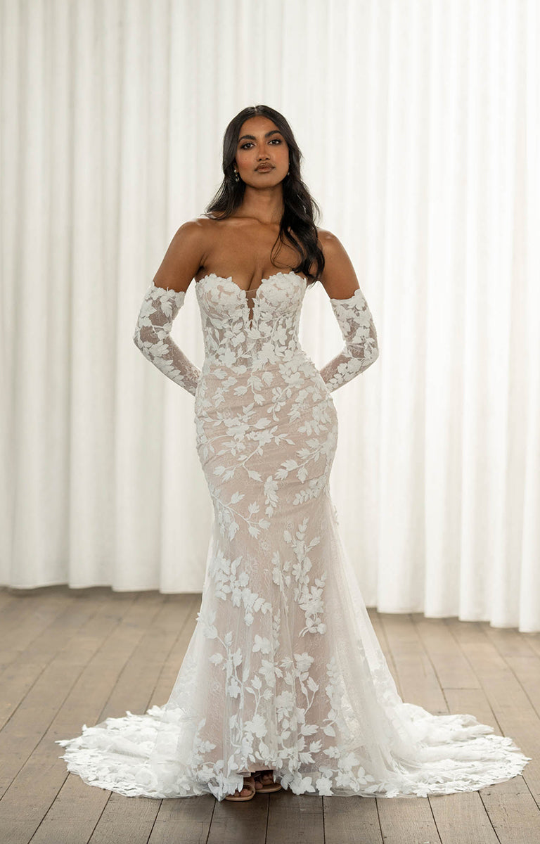 Woman wearing Thane by Madi Lane, a white lace wedding dress with long sleeves against a white curtain background