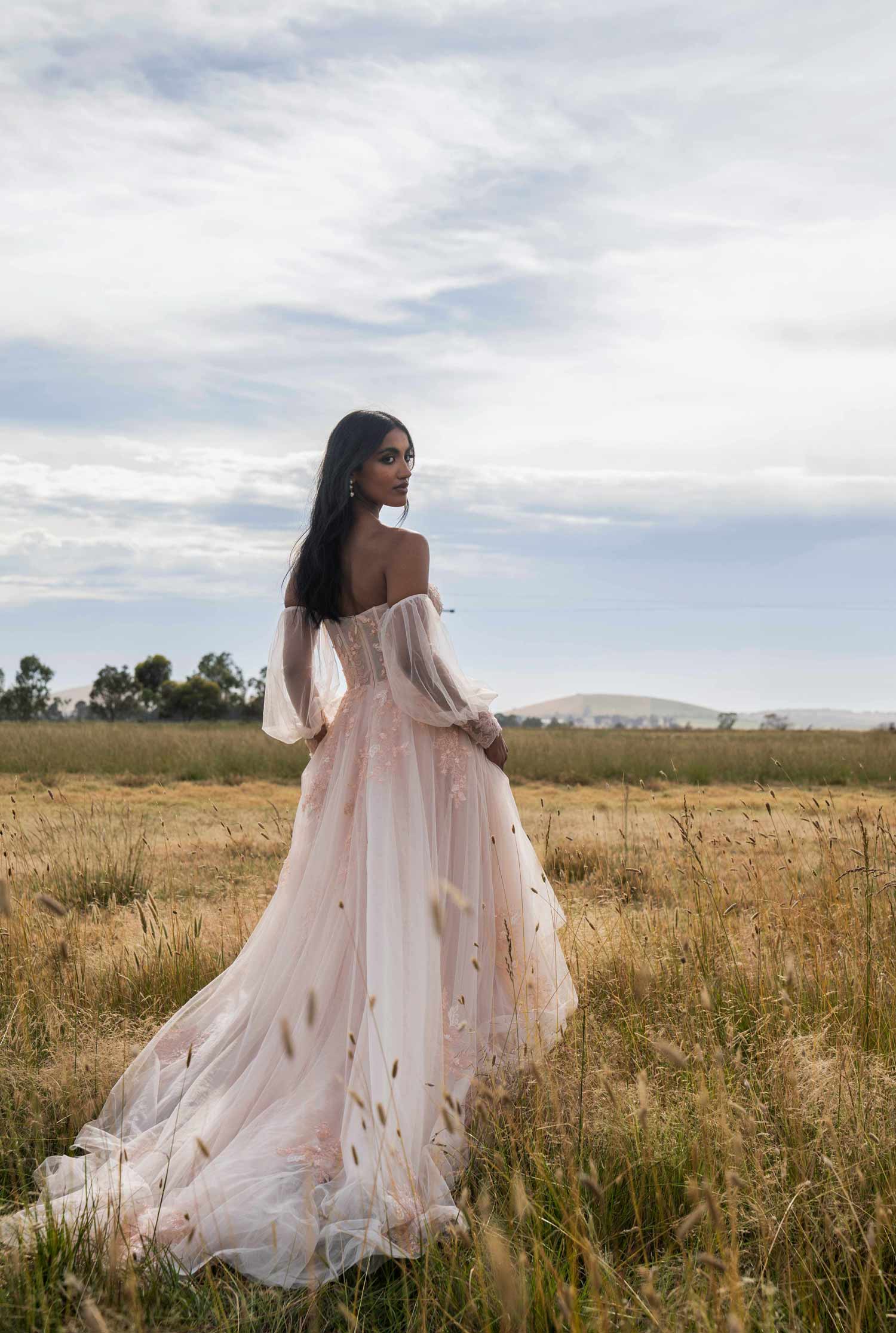 Woman in Turner by Madi Lane, a flowing dress standing in a field with a clear sky.
