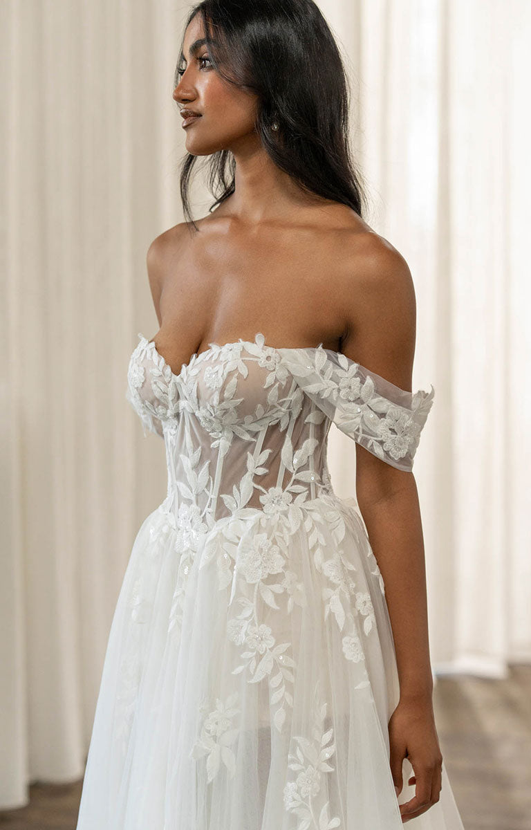 Woman wearing Twyla by Madi Lane, a white lace off-shoulder dress against a neutral background