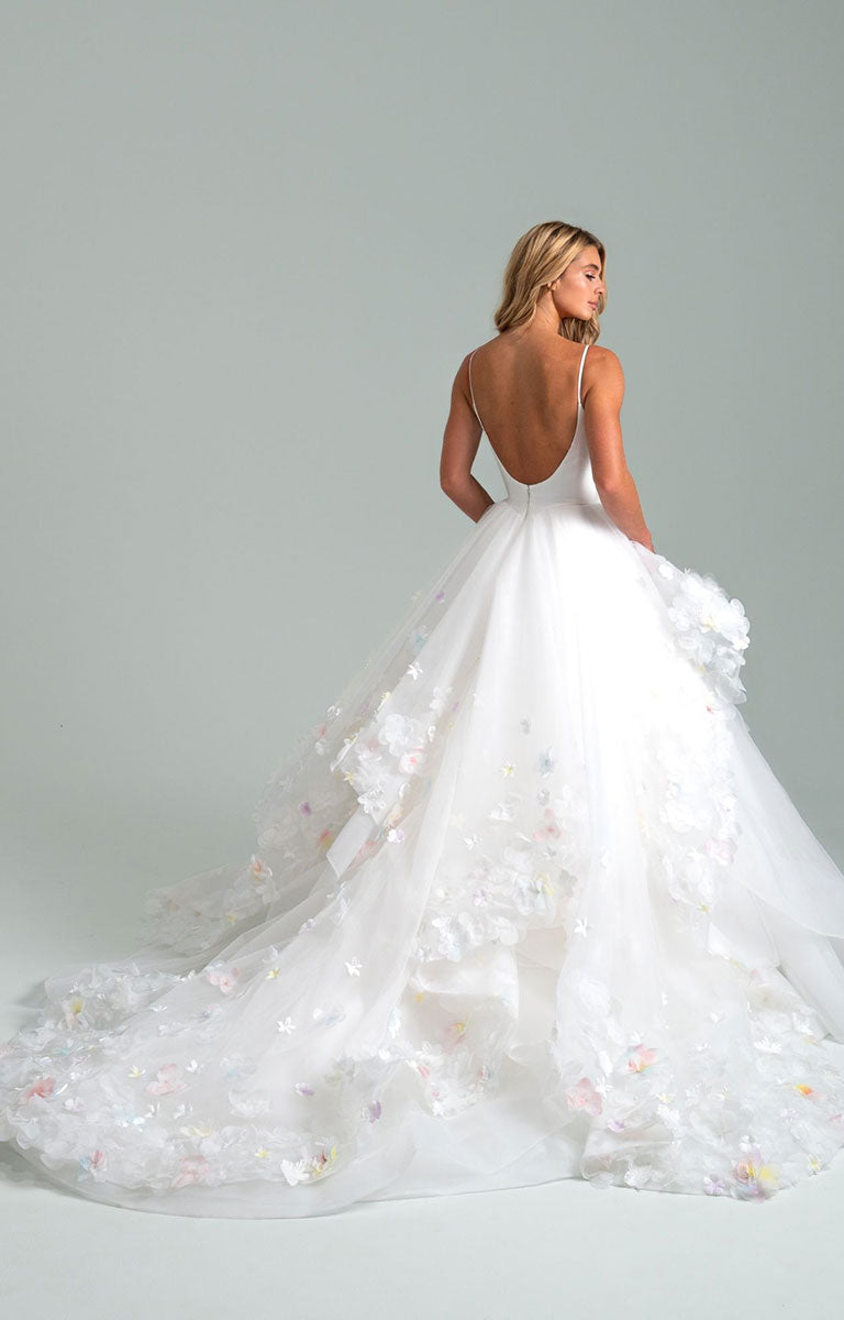 Woman wearing Turning Paiges by Hayley Paige - Layered Organza Ballgown Wedding Dress with a floral skirt on a plain background