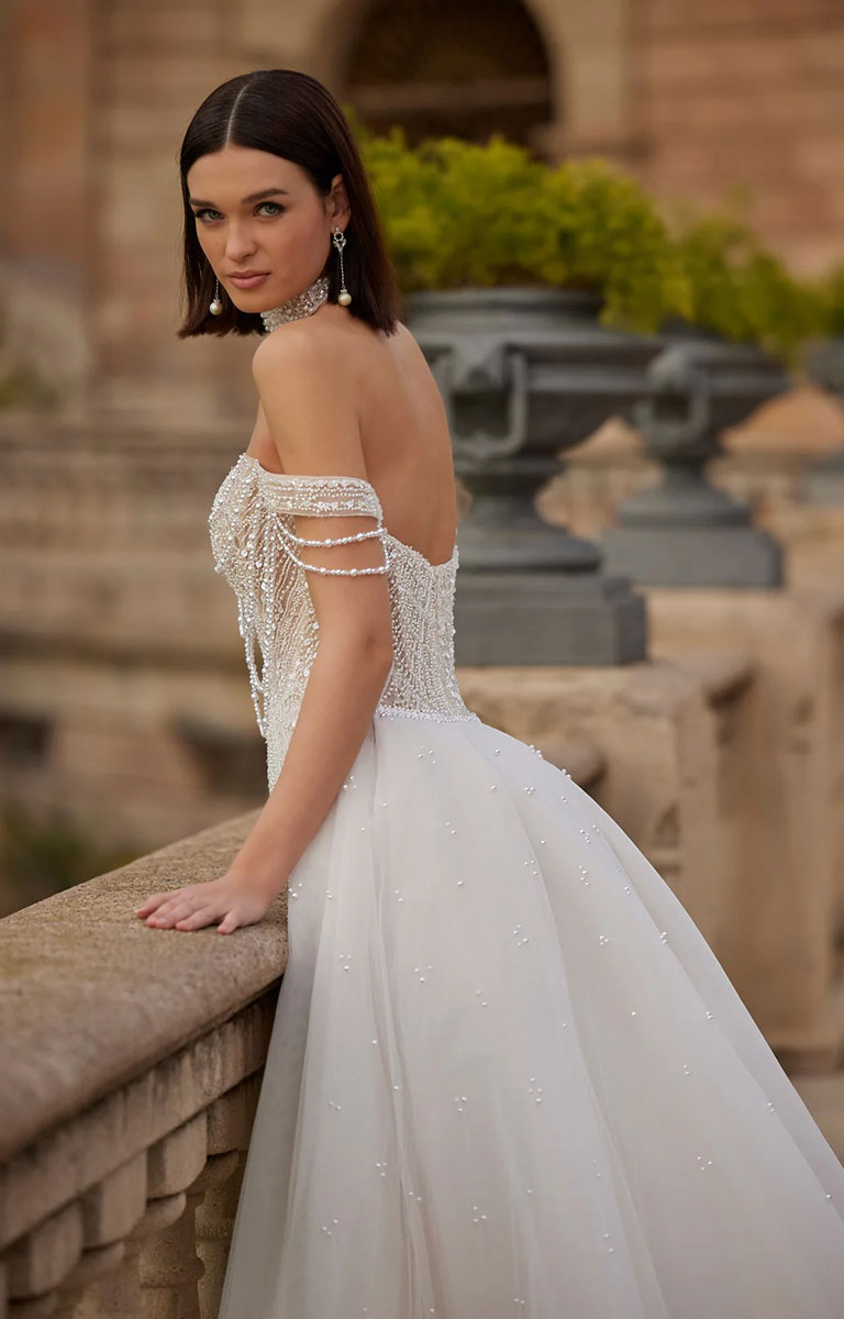 Woman in Helara by Veni Infantino Bridal - 1920s-Inspired Fit-and-Flare Wedding Dress with Pearl Beading with optional Overskirt standing outdoors with classical architecture in the background