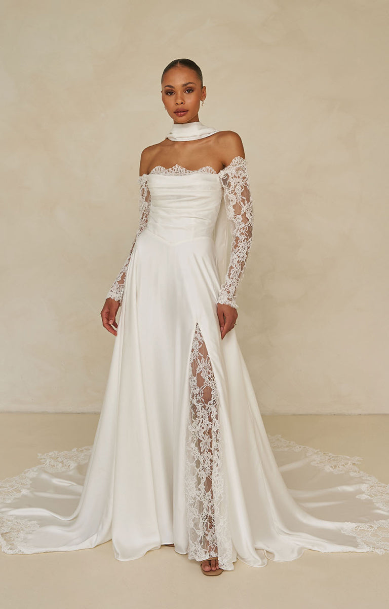 Ward by Madi Lane Bridal - White wedding dress with lace sleeves and a slit on a beige background