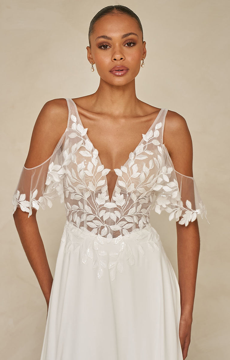 Woman wearing a Wilmott by Madi Lane - white lace wedding dress against a beige background
