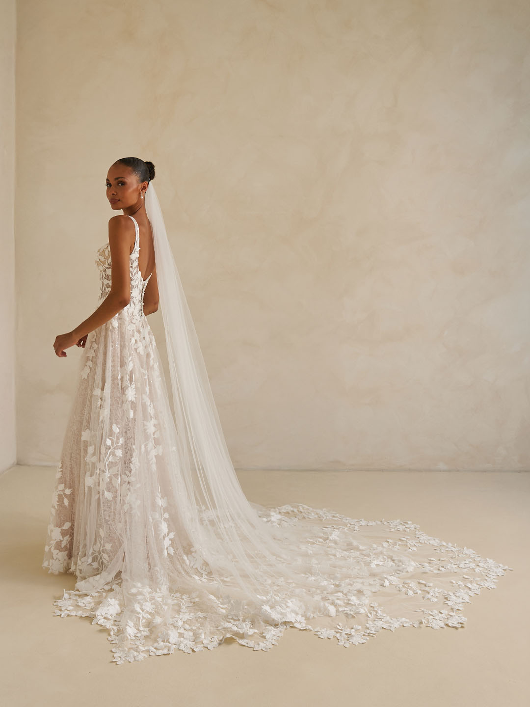 Bride in Wimmer by Madi Lane, a floral wedding dress with a long veil against a plain background
