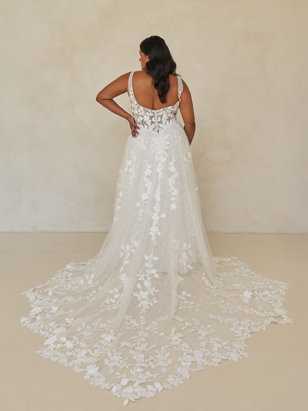 Woman wearing Wimmer by Madi Lane, a white lace wedding dress with floral details on a plain background
