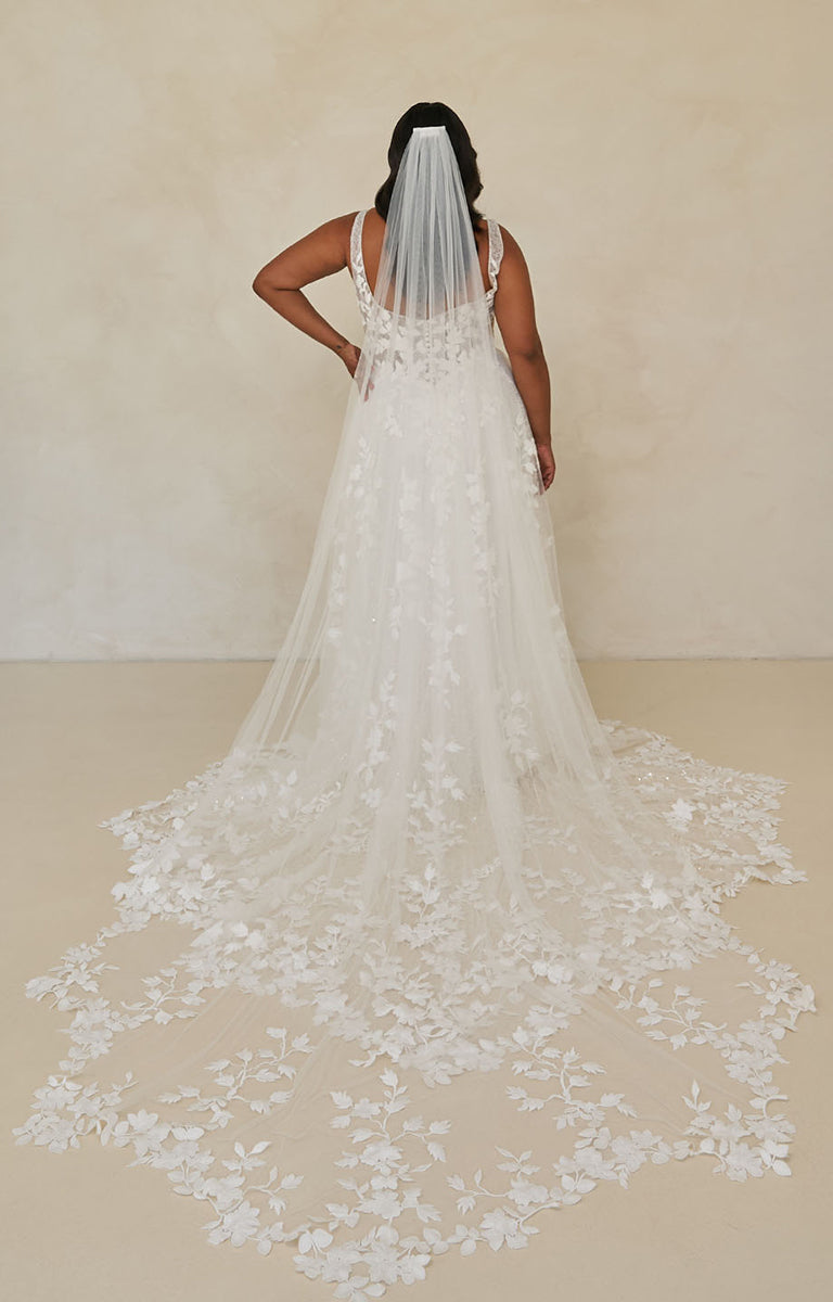 Bride wearing Wimmer by Madi Lane, a long, floral lace wedding dress with a matching veil against a plain background