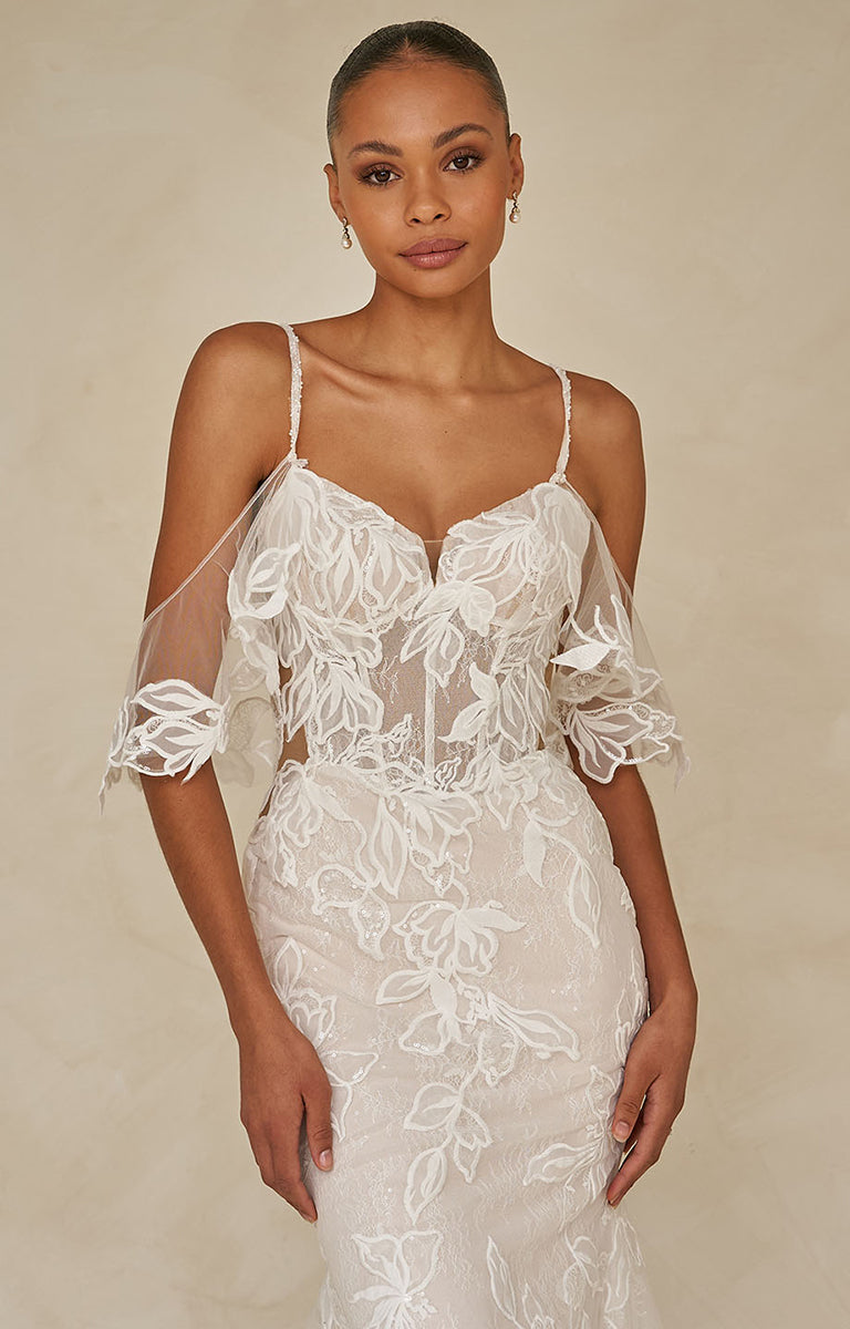 Woman wearing Winona by Madi Lane, a white lace wedding dress against a beige background