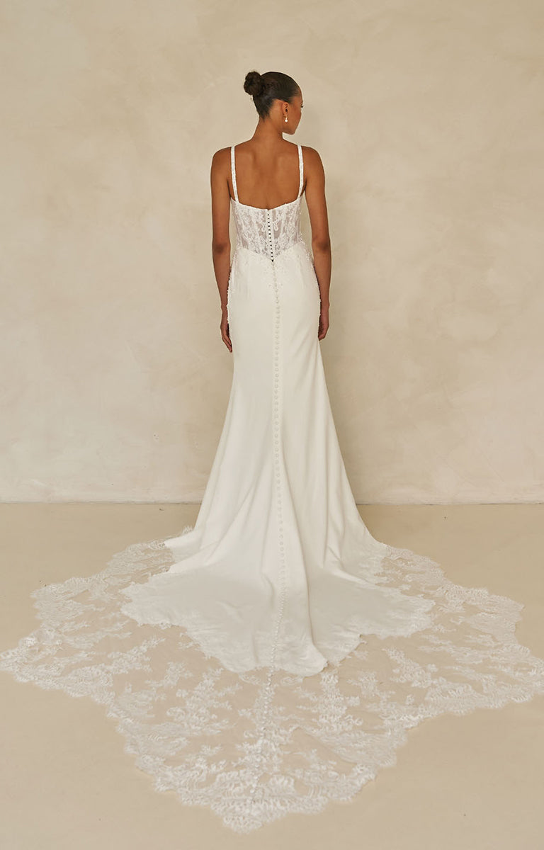 Woman wearing Wright by Madi Lane, a white lace wedding dress against a beige background