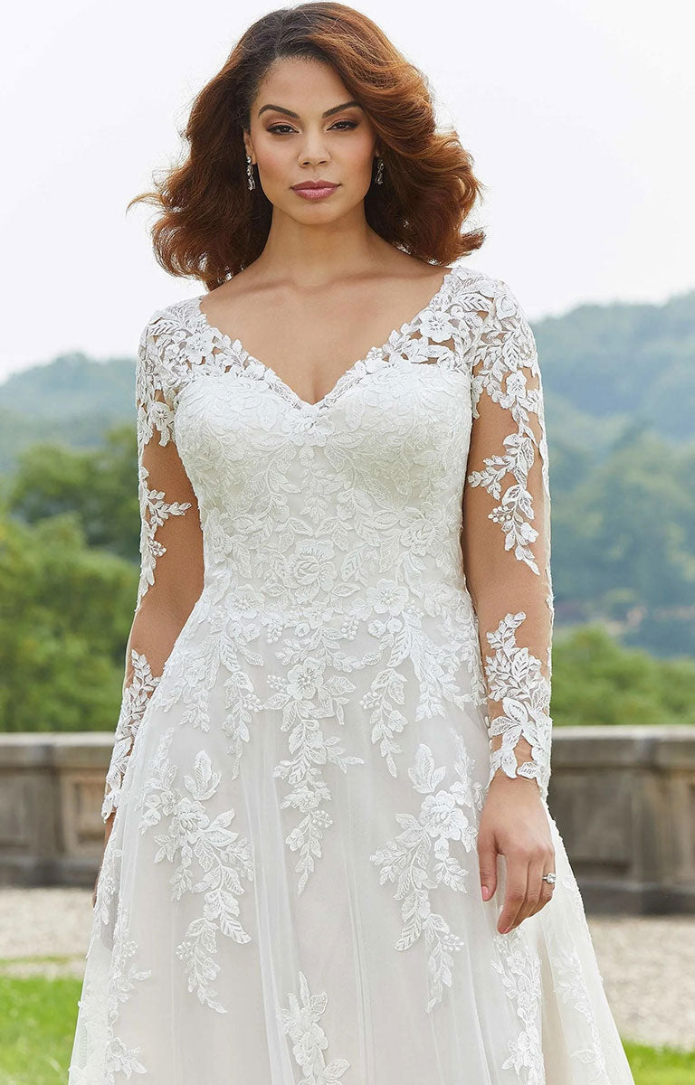 Woman wearing Emilia Wedding Dress by Morilee - Style 3346 – Floral Lace A-Line Gown with Illusion Sleeves with a scenic background