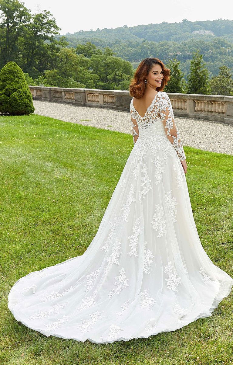 Woman in Emilia Wedding Dress by Morilee - Style 3346 – Floral Lace A-Line Gown with Illusion Sleeves standing on grass with trees in the background