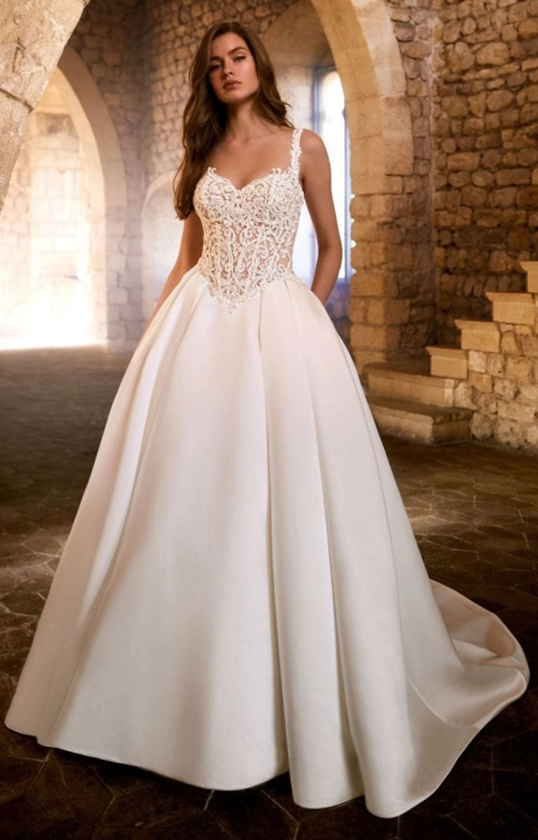 A woman modeling Glorielle by Étoile Bridal - Satin Ballgown Wedding Dress with Sweetheart Neckline and Royal Train with a lace-embellished sweetheart bodice and a full satin skirt, standing in a stone archway interior.