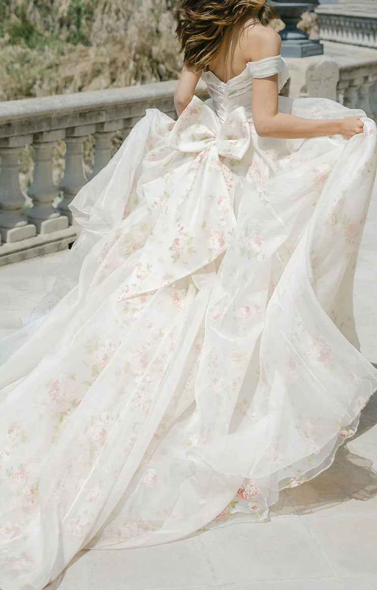 Woman in Constance by Josephine Scott - Silk Organza Ballgown Wedding Dress with Rose Print and Detachable Bow, standing on a stone staircase.
