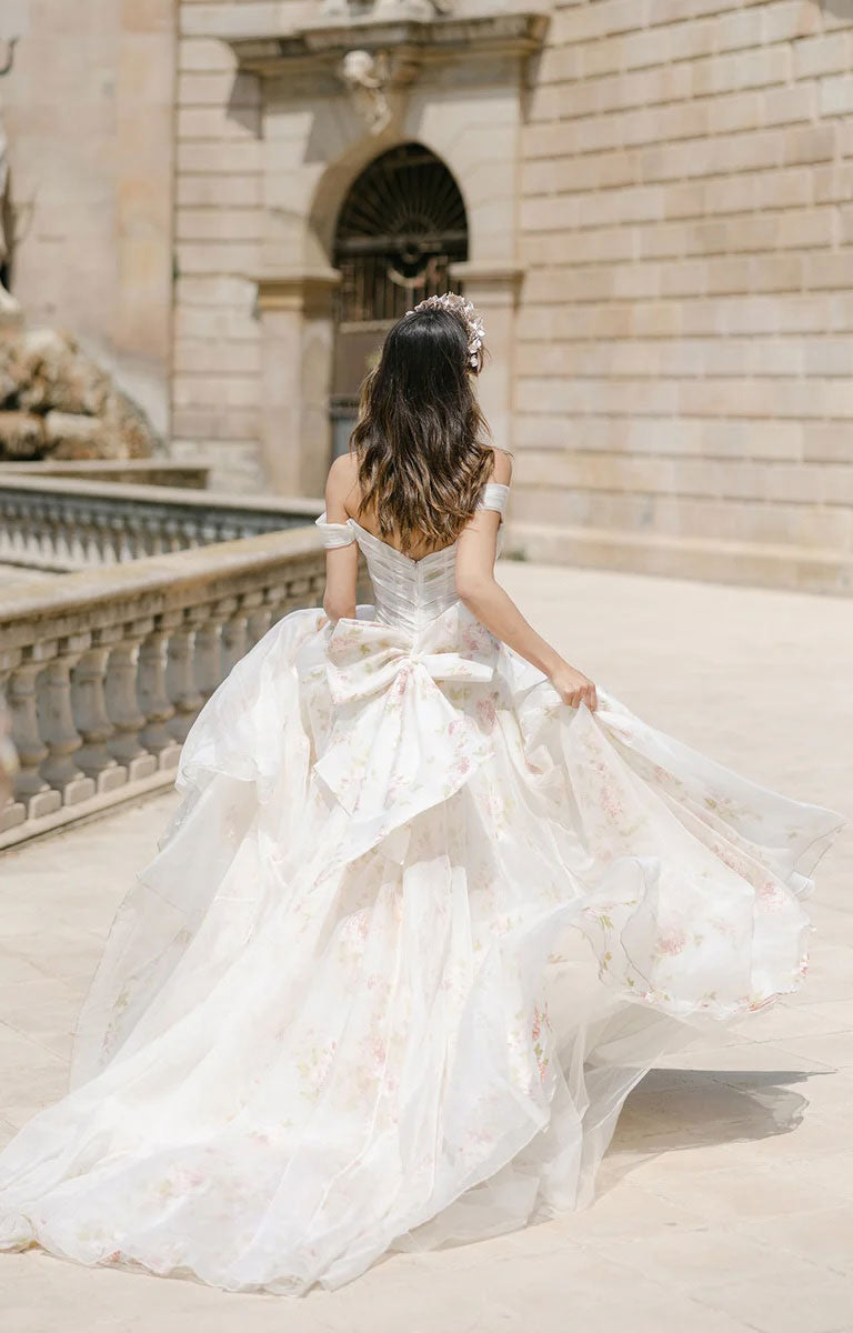 Woman in Constance by Josephine Scott - Silk Organza Ballgown Wedding Dress with Rose Print and Detachable Bow standing in front of a classical building.