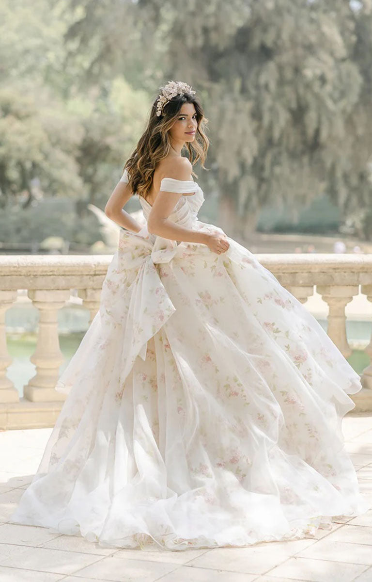 Woman in Constance by Josephine Scott - Silk Organza Ballgown Wedding Dress with Rose Print and Detachable Bow standing outdoors with greenery in the background