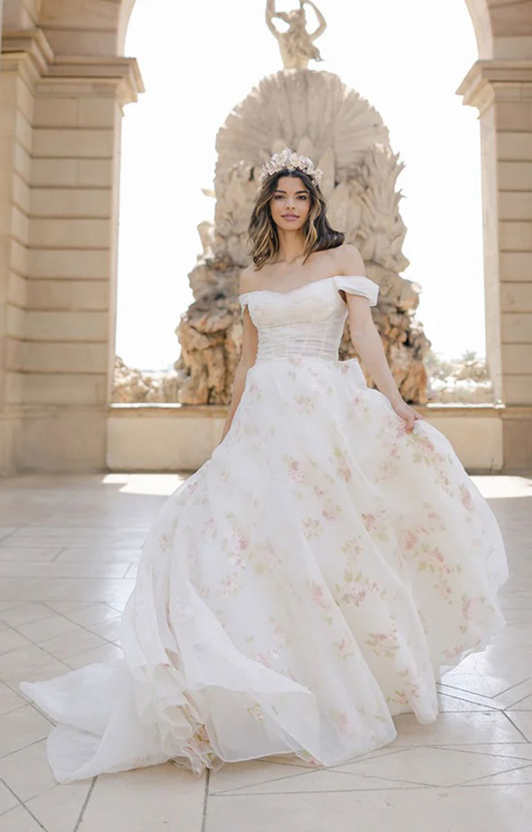 Woman in Constance by Josephine Scott - Silk Organza Ballgown Wedding Dress with Rose Print and Detachable Bow standing in front of an ornate throne-like chair.