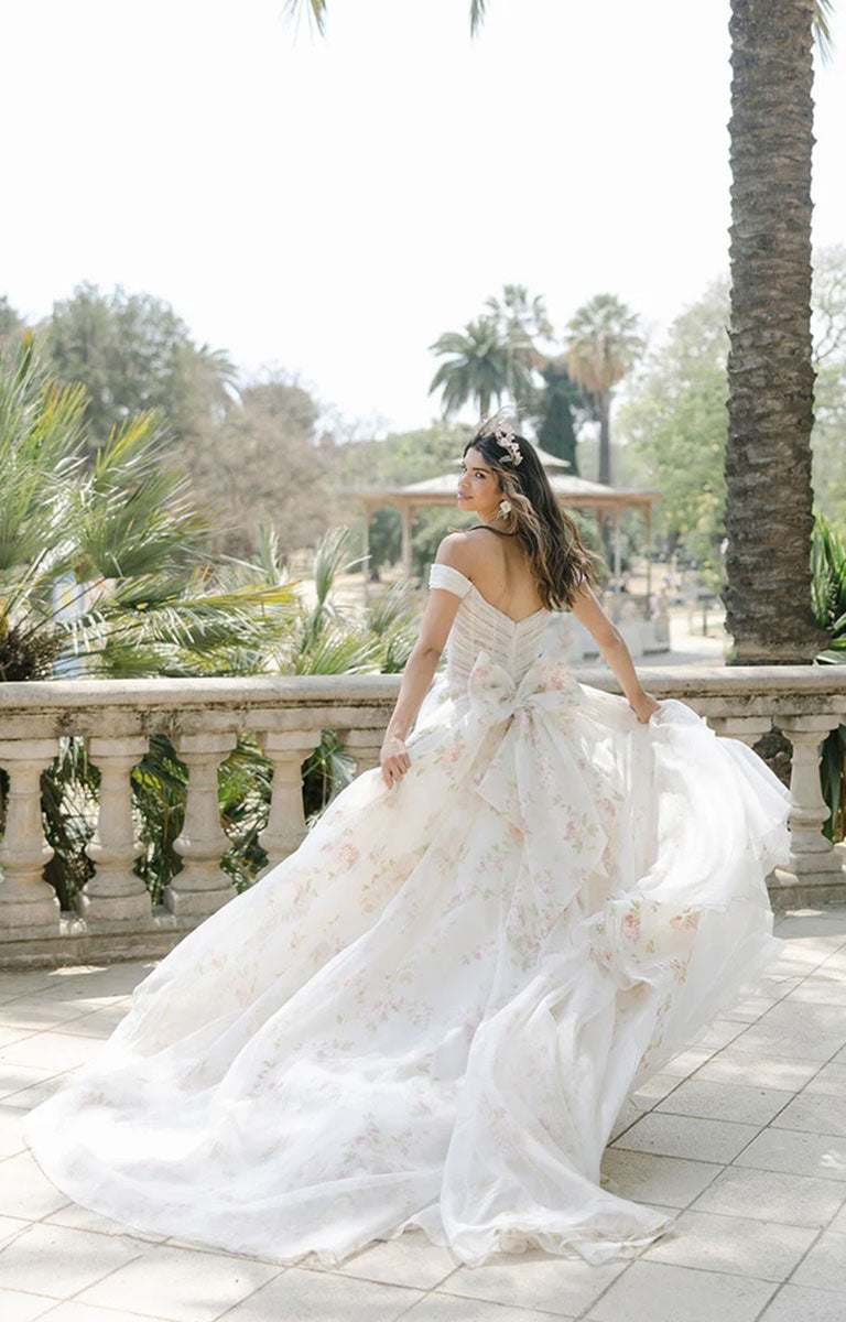 Woman in Constance by Josephine Scott - Silk Organza Ballgown Wedding Dress with Rose Print and Detachable Bow standing outdoors with palm trees in the background