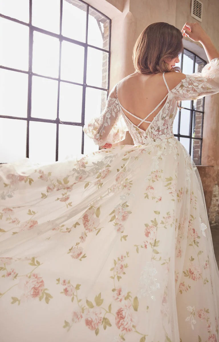 Woman wearing Elora by Josephine Scott - Romantic Rose Print Ballgown Wedding Dress with Lace Appliqué and Voluminous Bell Sleeves with a large window in the background