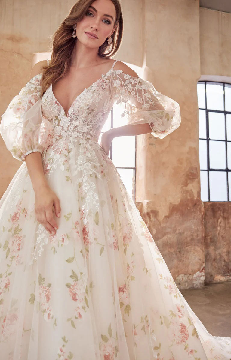 Woman wearing Elora by Josephine Scott - Romantic Rose Print Ballgown Wedding Dress with Lace Appliqué and Voluminous Bell Sleeves in an indoor setting with a rustic background.