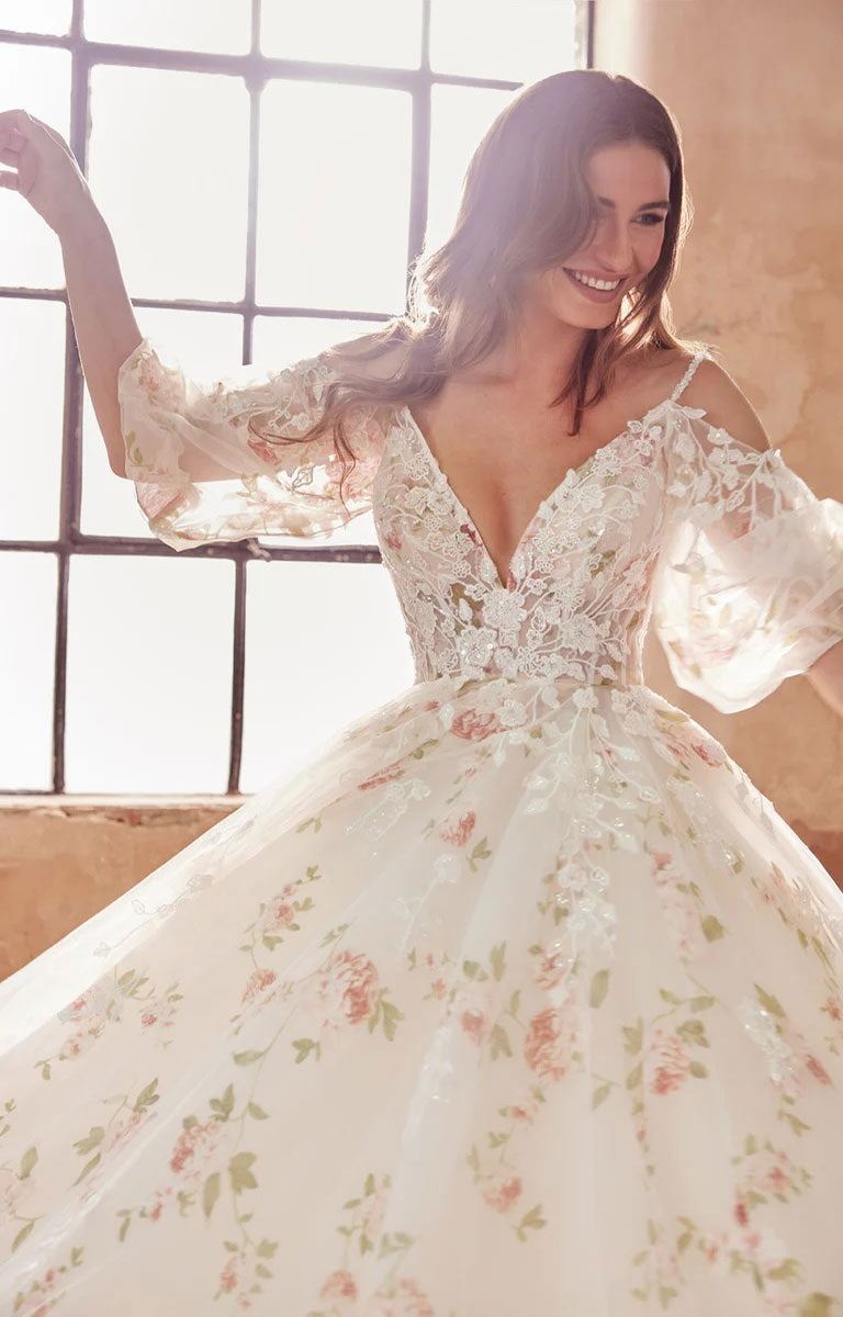 Woman wearing Elora by Josephine Scott - Romantic Rose Print Ballgown Wedding Dress with Lace Appliqué and Voluminous Bell Sleeves with a large window in the background