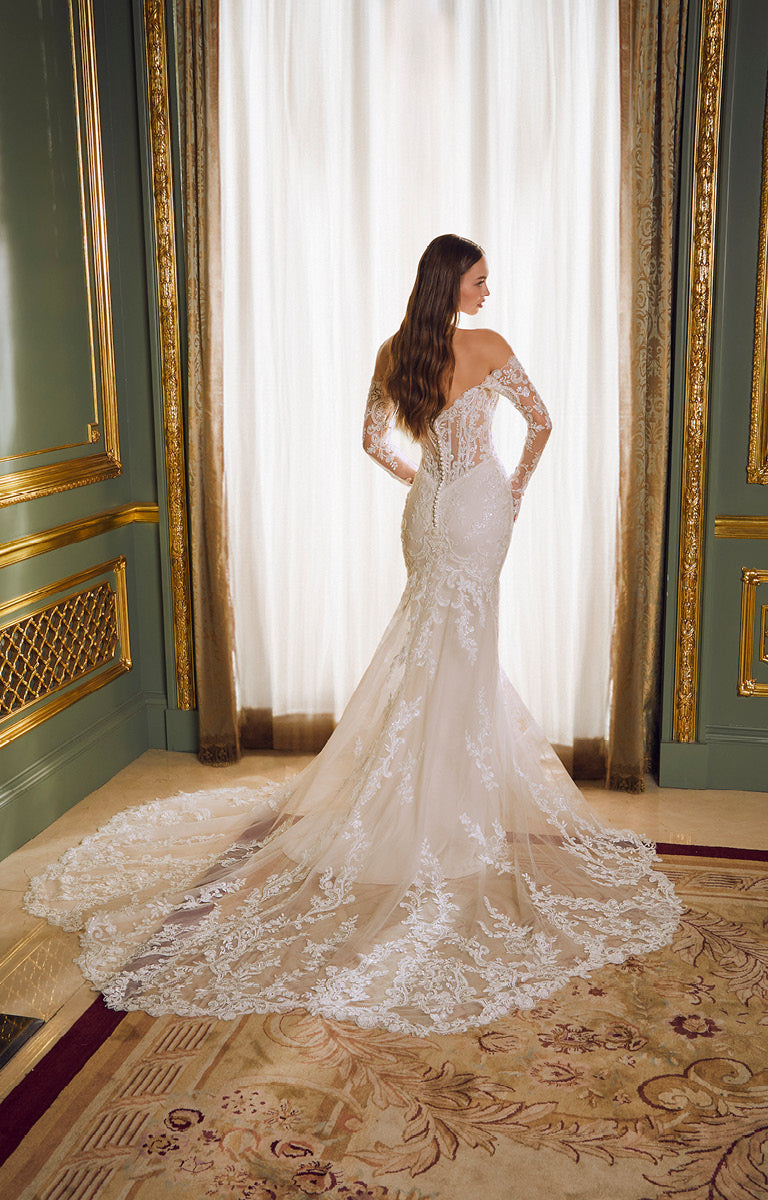 Woman in a white lace wedding dress standing in a room with ornate decor.