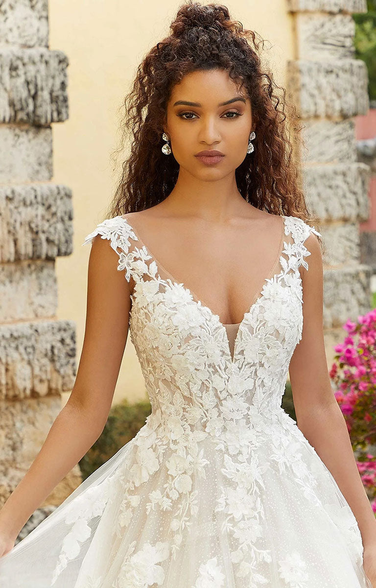 Woman wearing Fiorenza by Morilee - Romantic Lace and Glitter Tulle Wedding Dress with Sculpted Bodice with a stone wall and flowers in the background