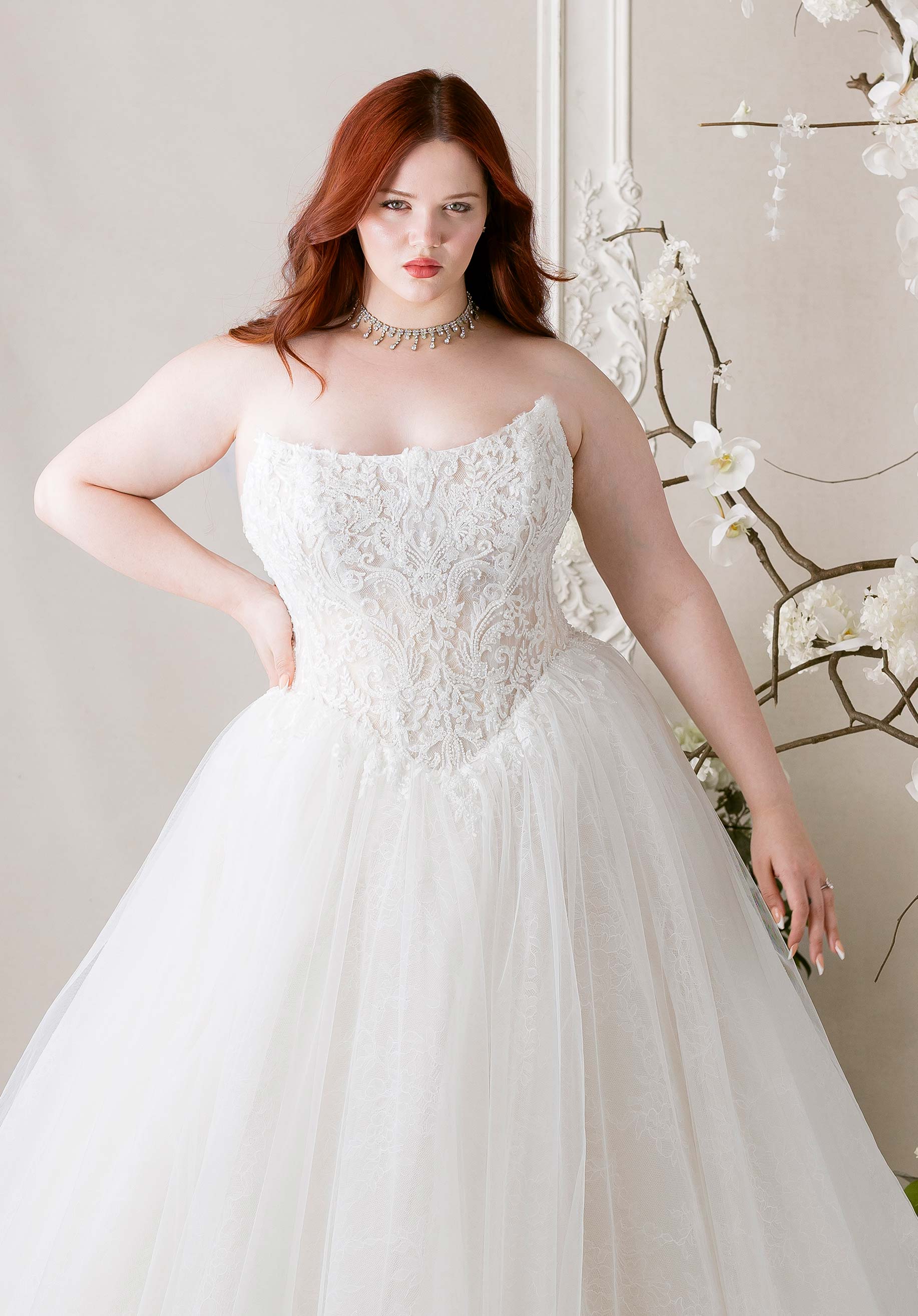 Woman wearing Meli by Morilee - Plus-Size Ball Gown with Detachable Off-the-Shoulder Sleeves with floral lace details, standing against a neutral background.