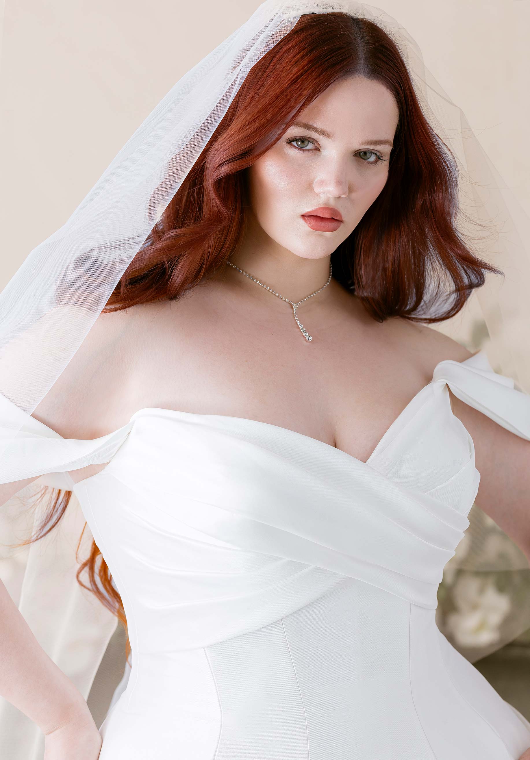 Woman in Kalina by Morilee - Ball Gown with Cat-Eye Neckline and Detachable Off-the-Shoulder Sleeves with a veil against a neutral background