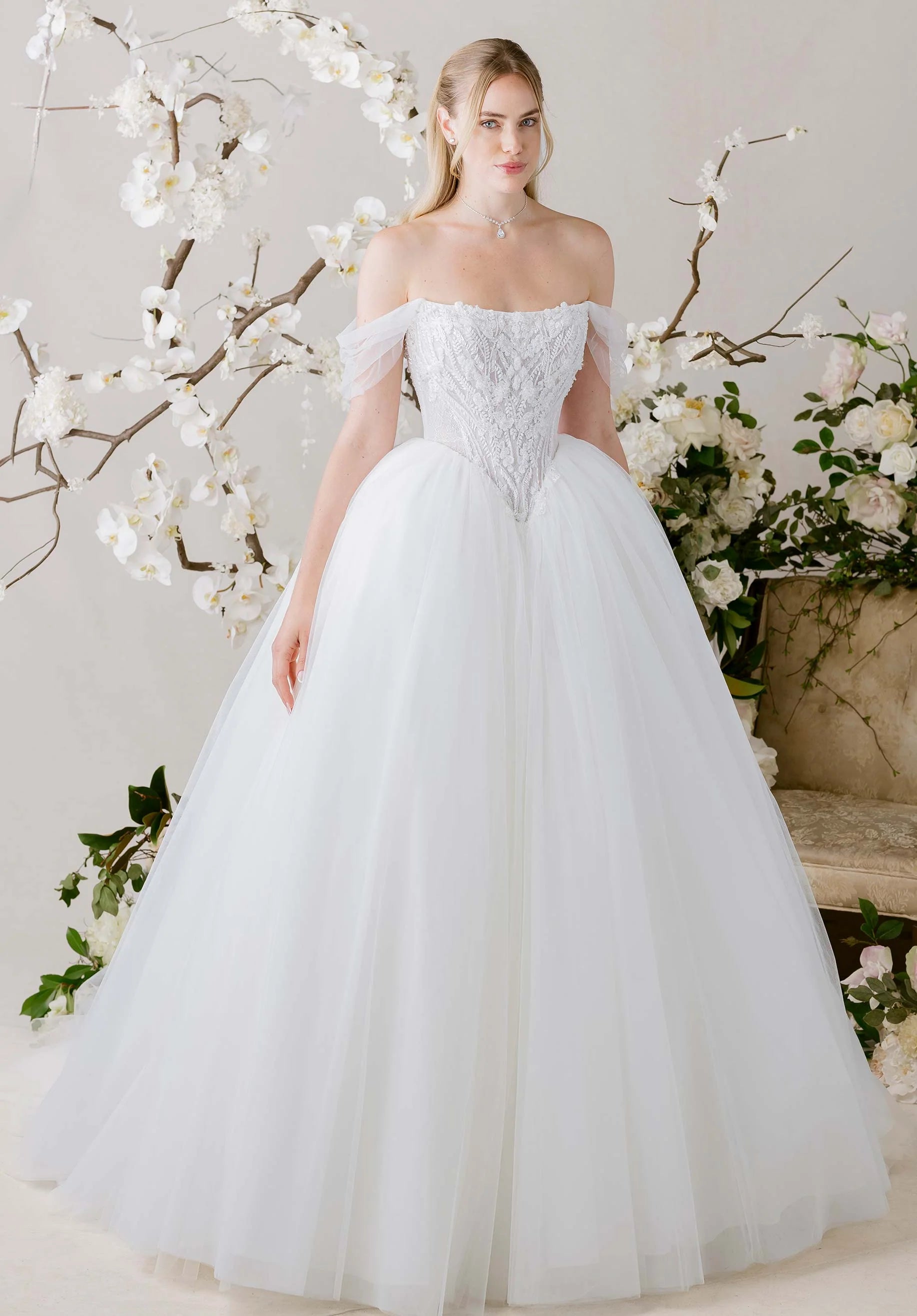 Woman in Virtuoso by Morilee - Ball Gown with Scoop Neckline and Botanical Beading standing in front of floral decorations