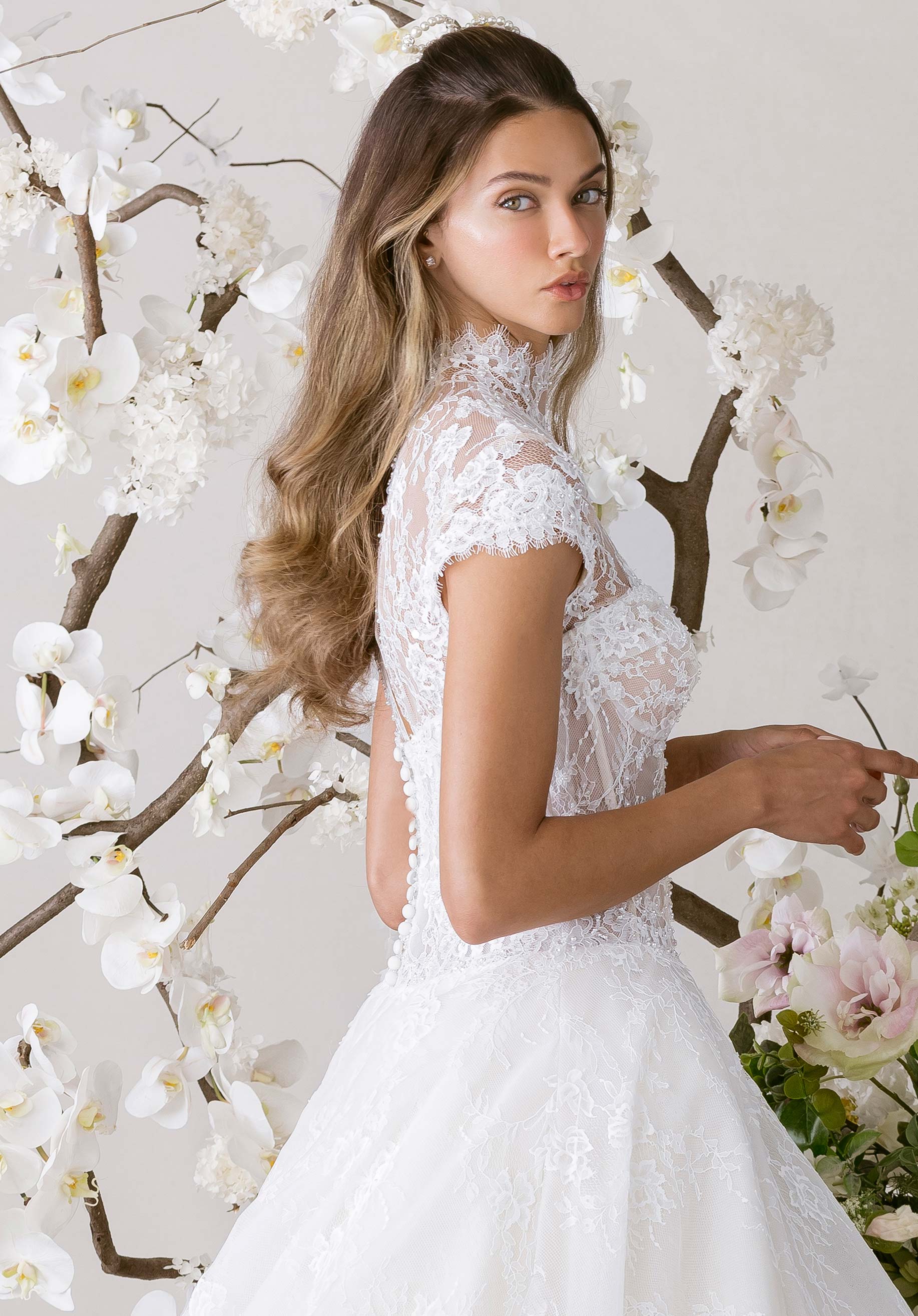 Woman in a white lace dress standing against a floral and branch backdrop
