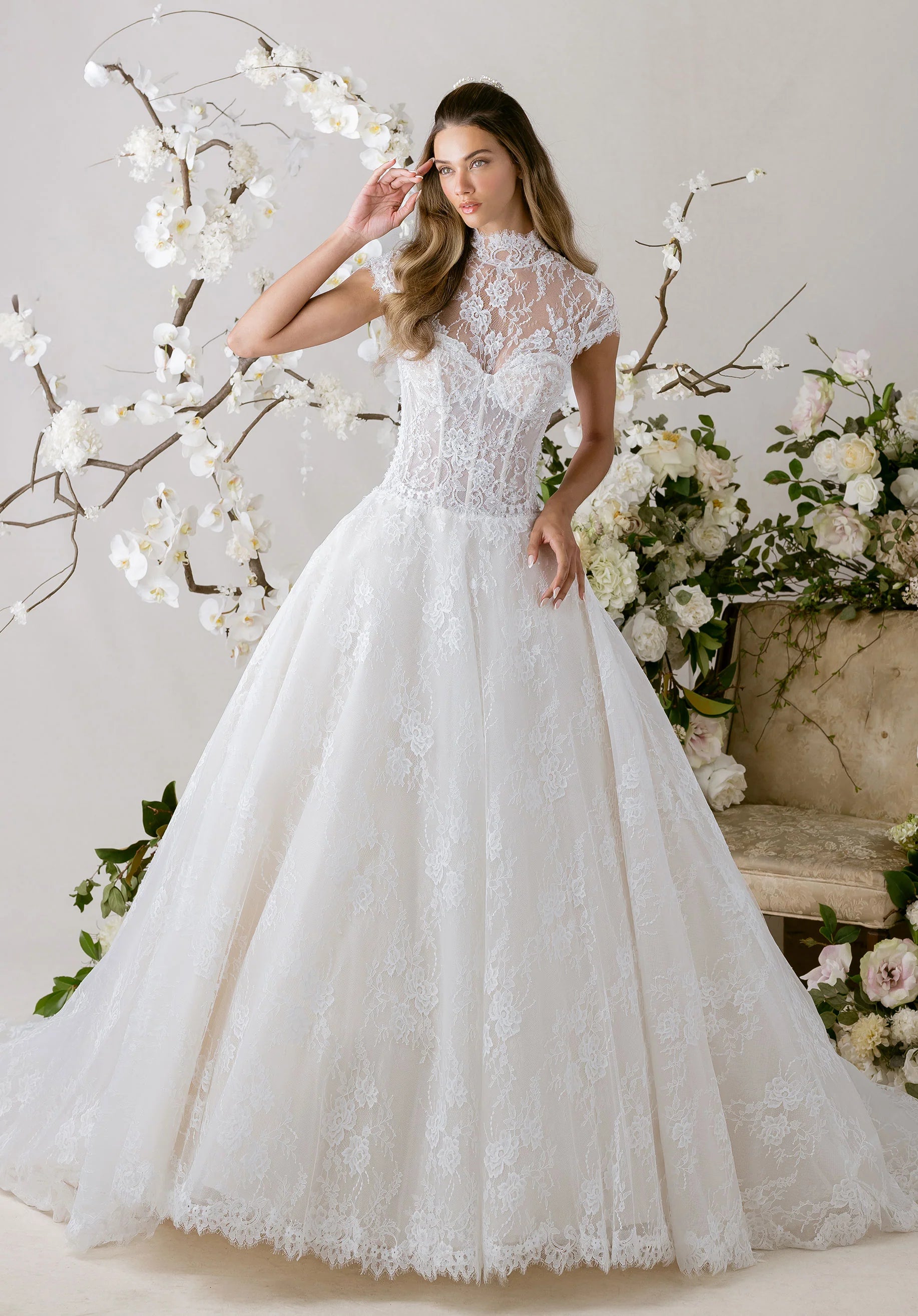 Woman in a white lace wedding dress standing in front of floral decorations.