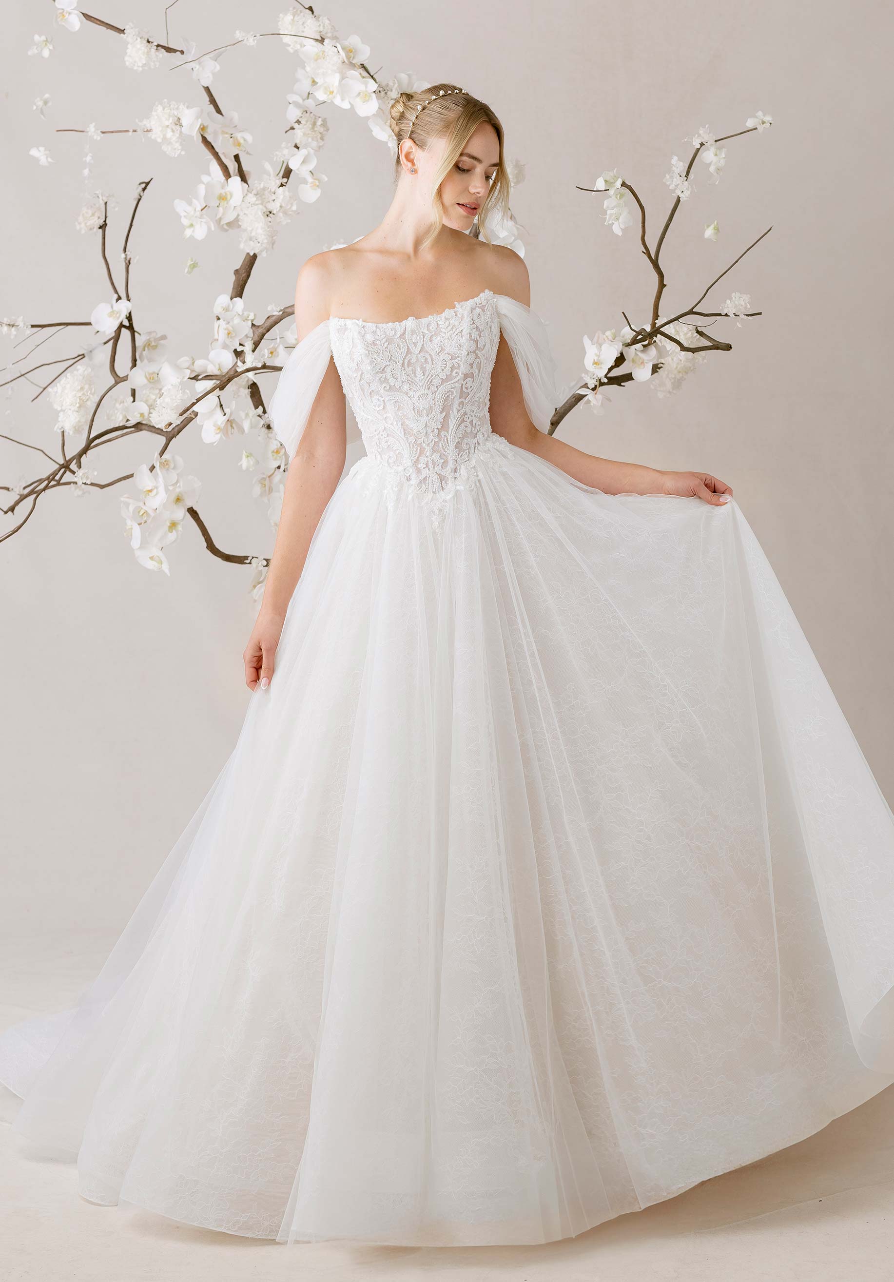Woman in a white wedding dress standing next to white floral branches on a neutral background