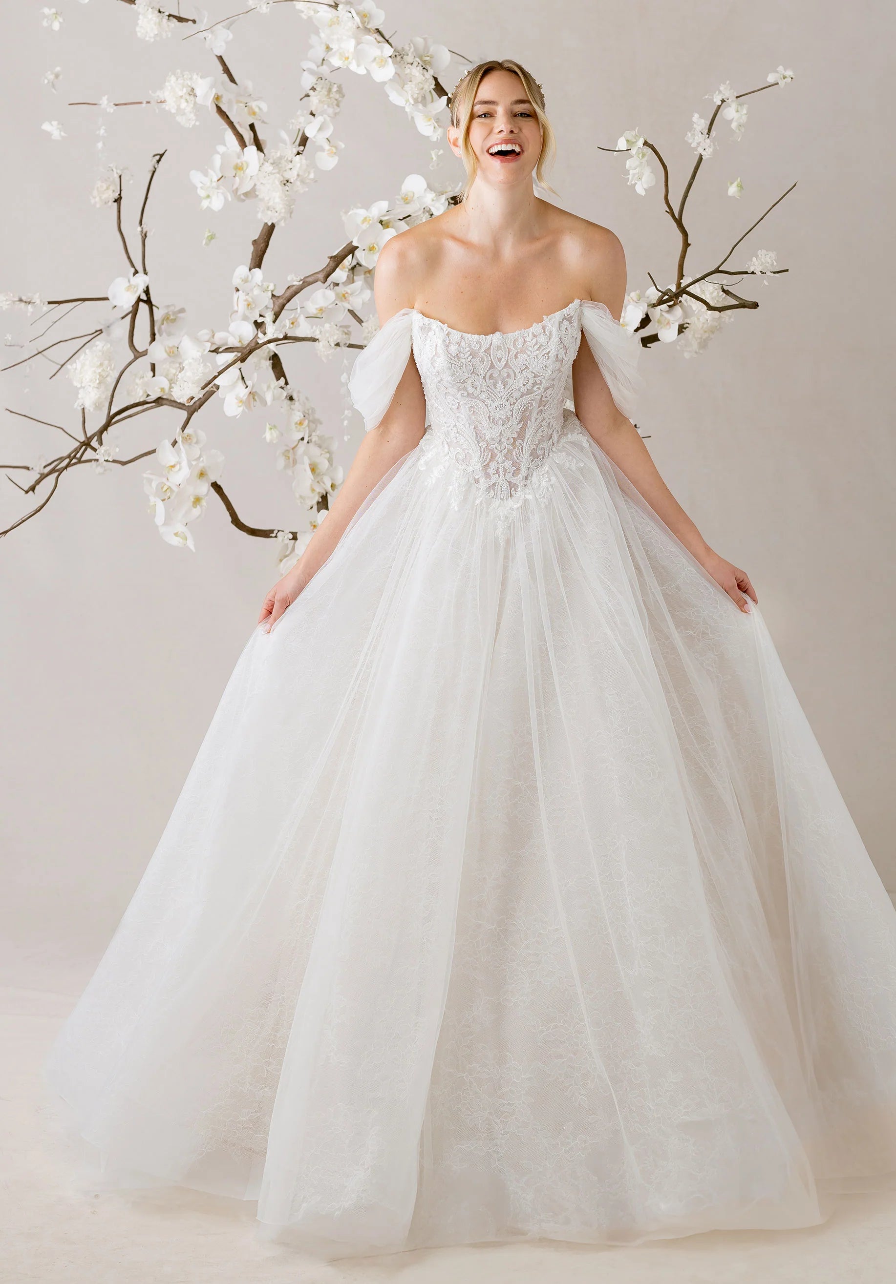 Woman in a white wedding dress standing next to white floral branches against a light background