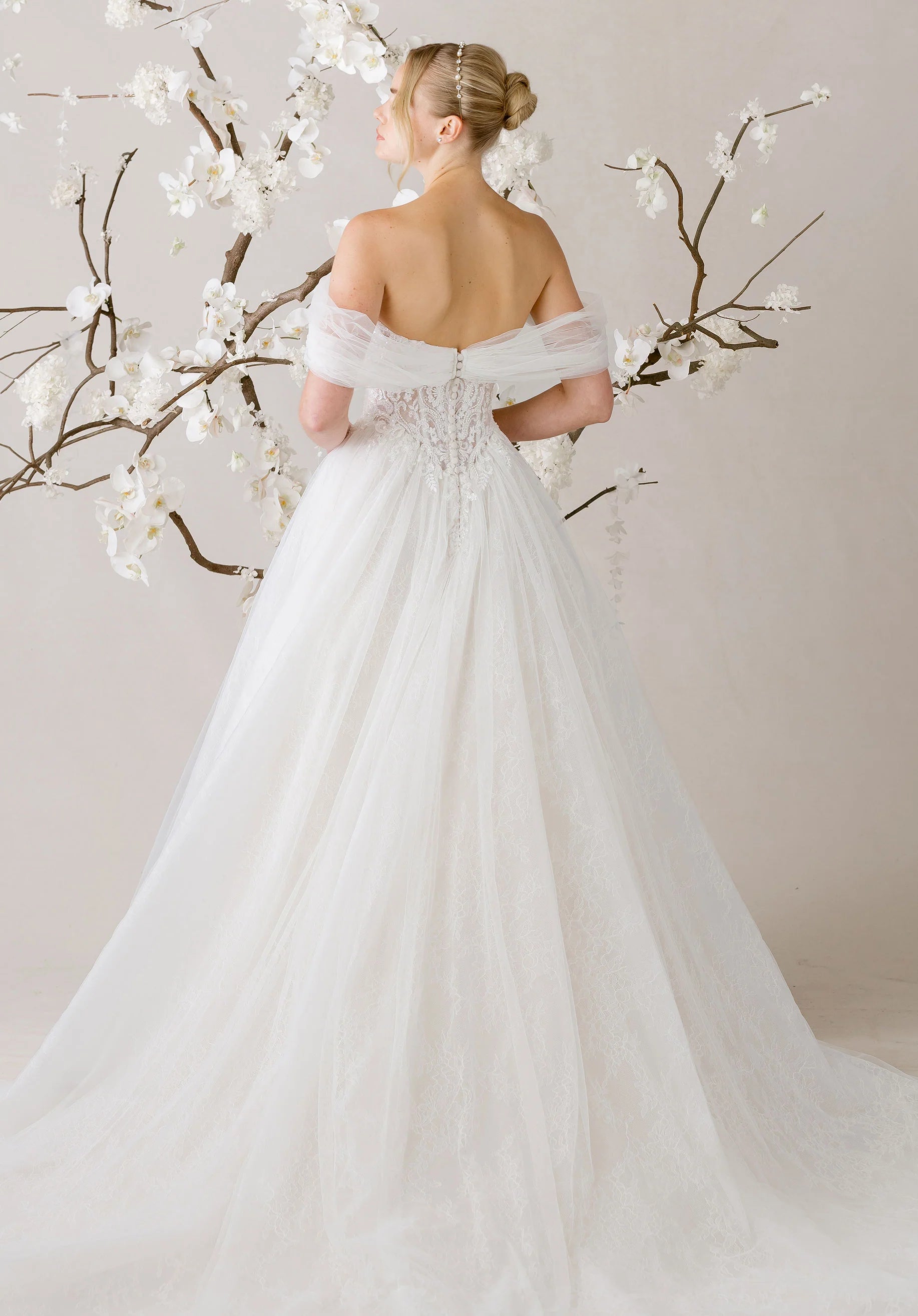 Woman in a white wedding dress standing in front of cherry blossom branches.