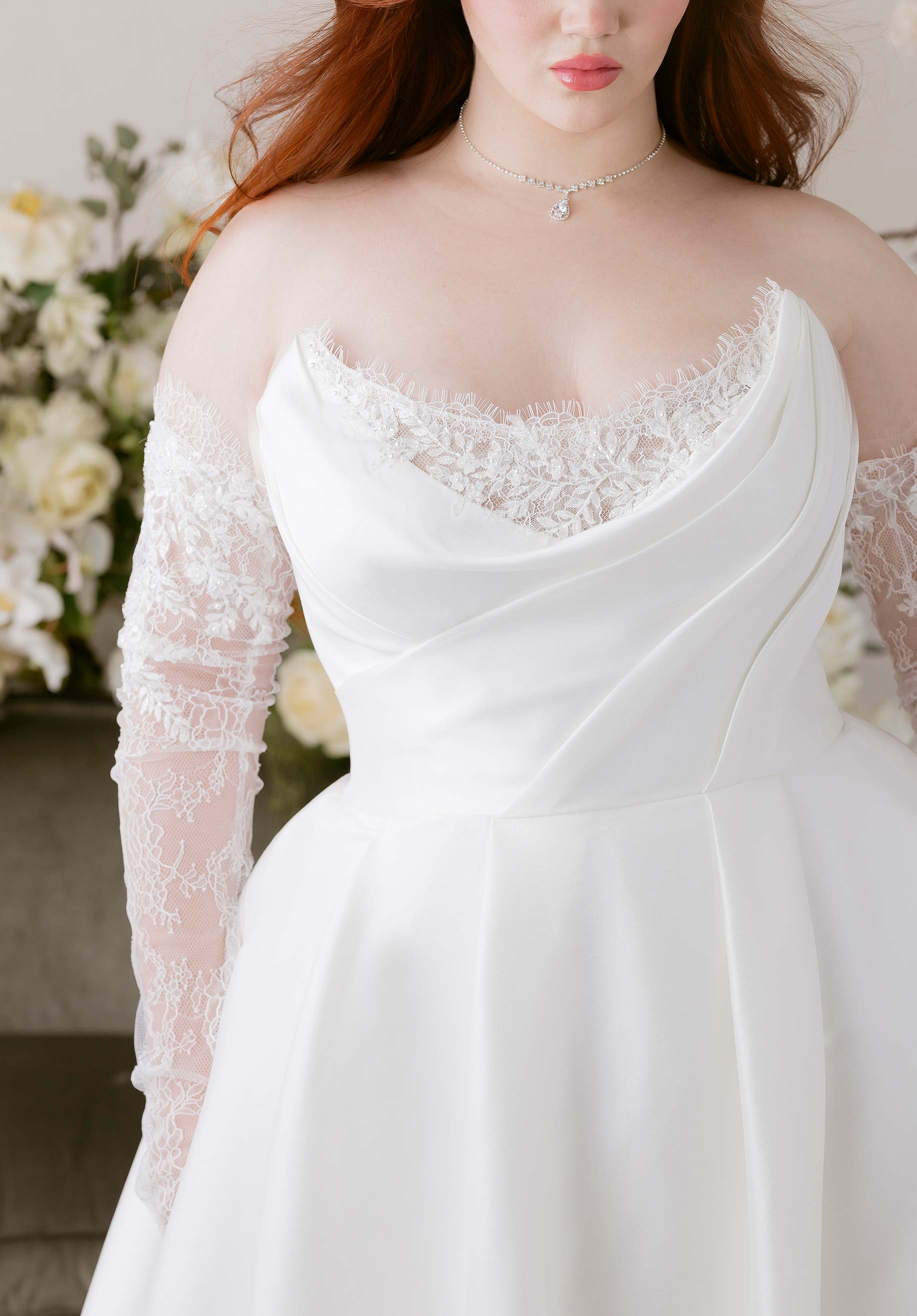 Close-up of a person wearing a white wedding dress with lace sleeves and neckline.