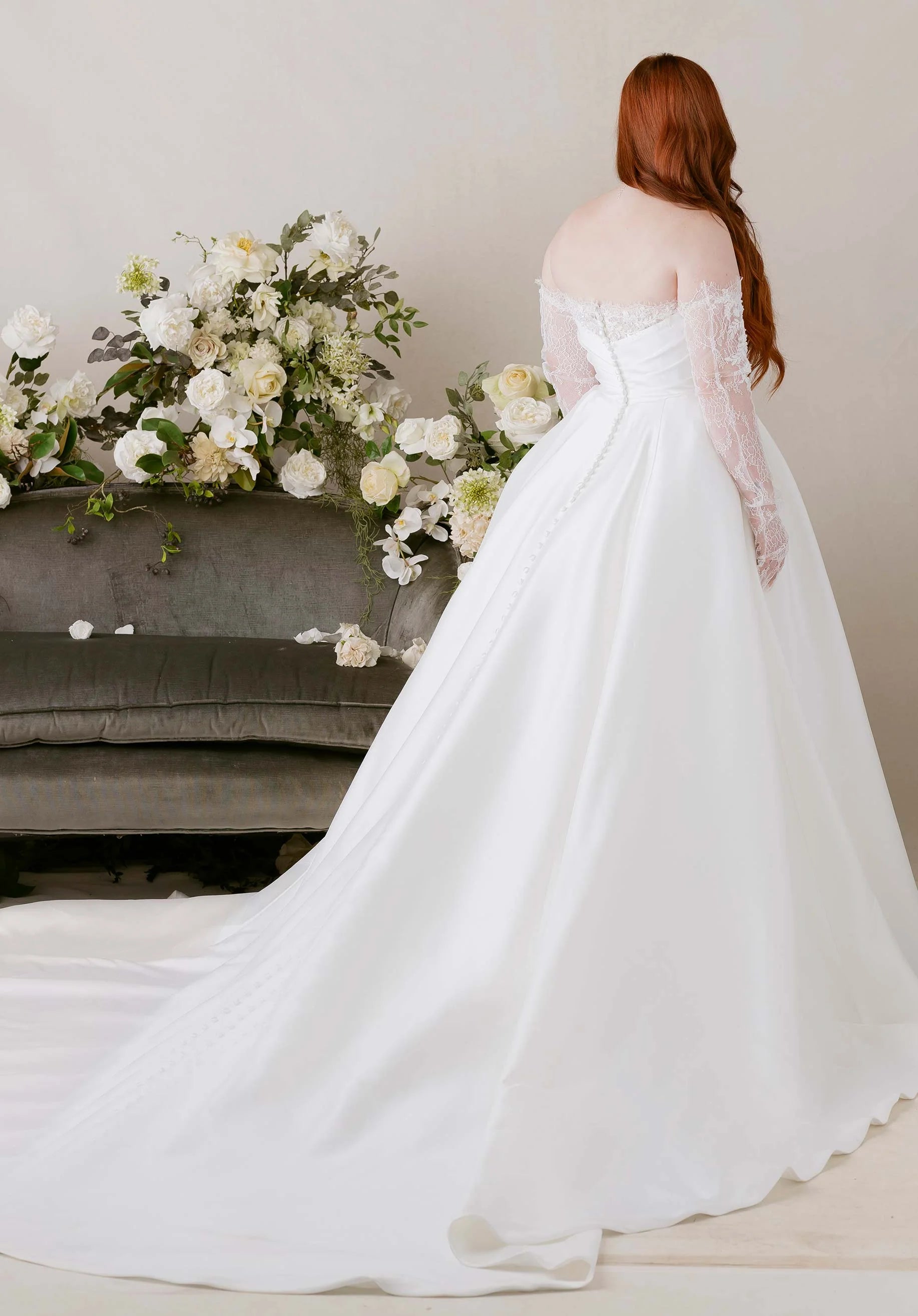 Woman in a white wedding dress standing in front of floral arrangements.