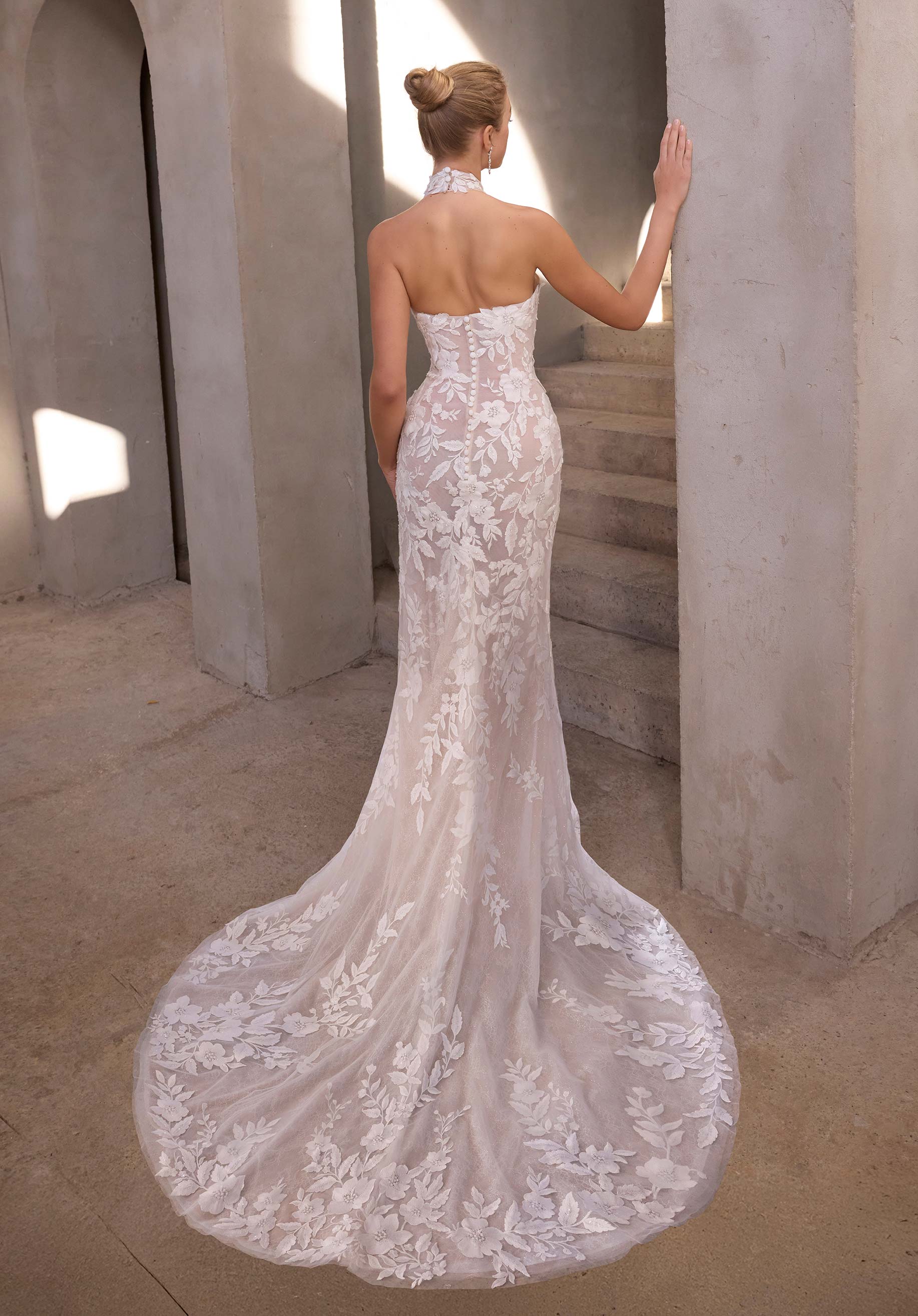 Woman in a white lace wedding dress standing in a sunlit hallway.