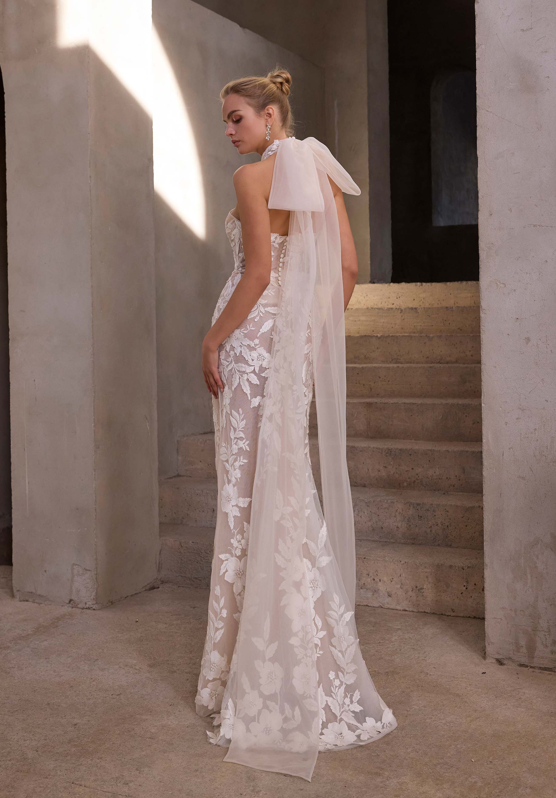 Woman in a white lace wedding dress with a cape in an indoor setting.