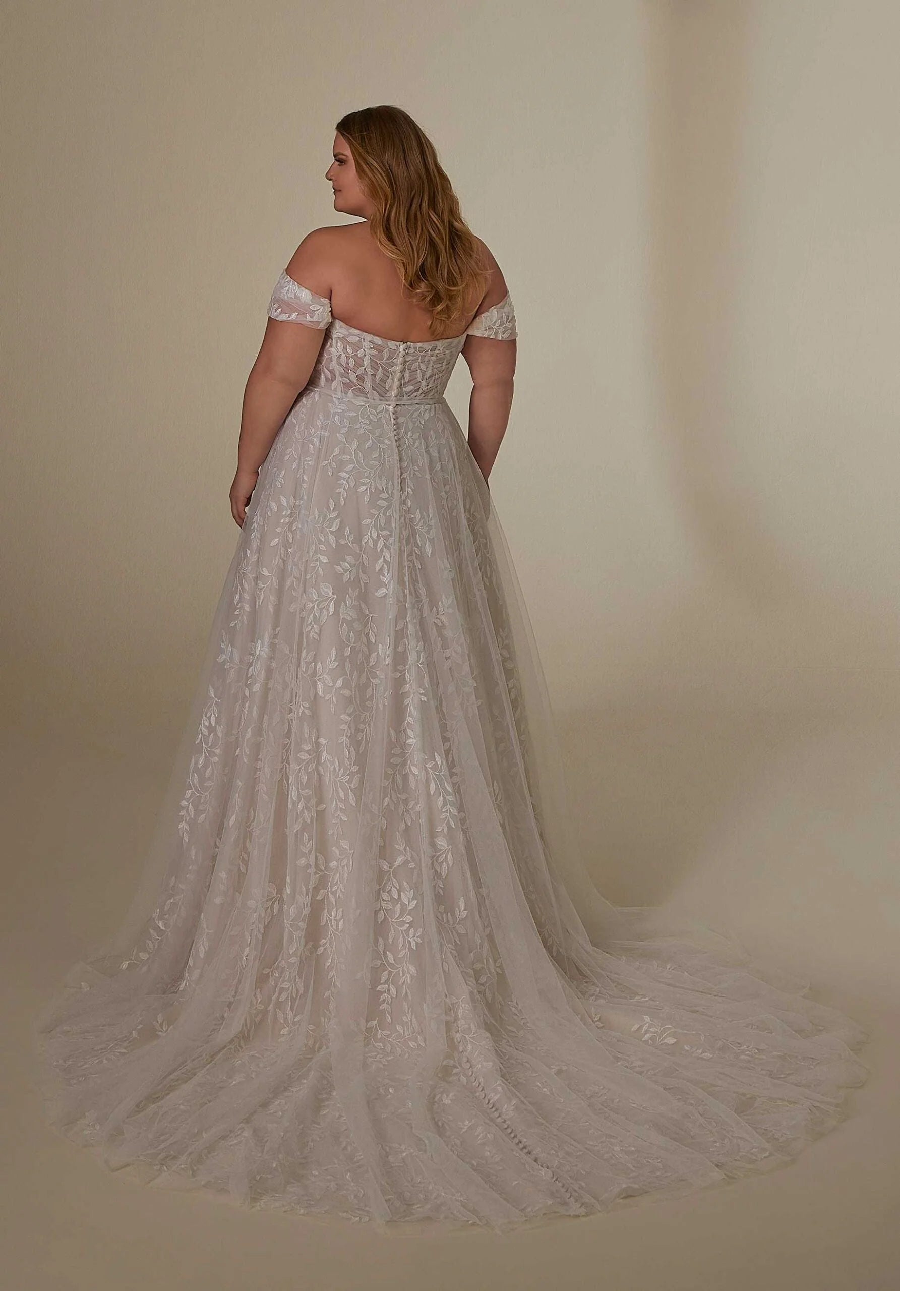 Woman wearing a lace wedding dress with a long train on a plain background