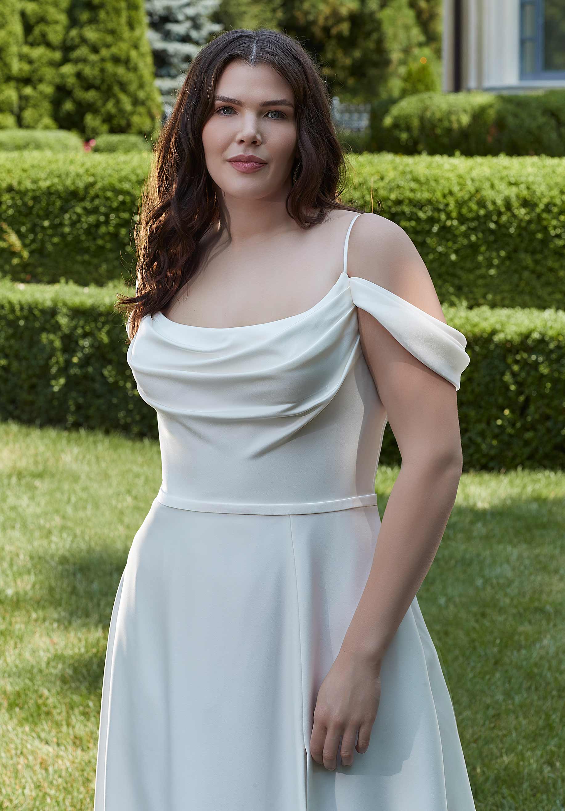 Woman in a white off-shoulder dress standing in a garden.