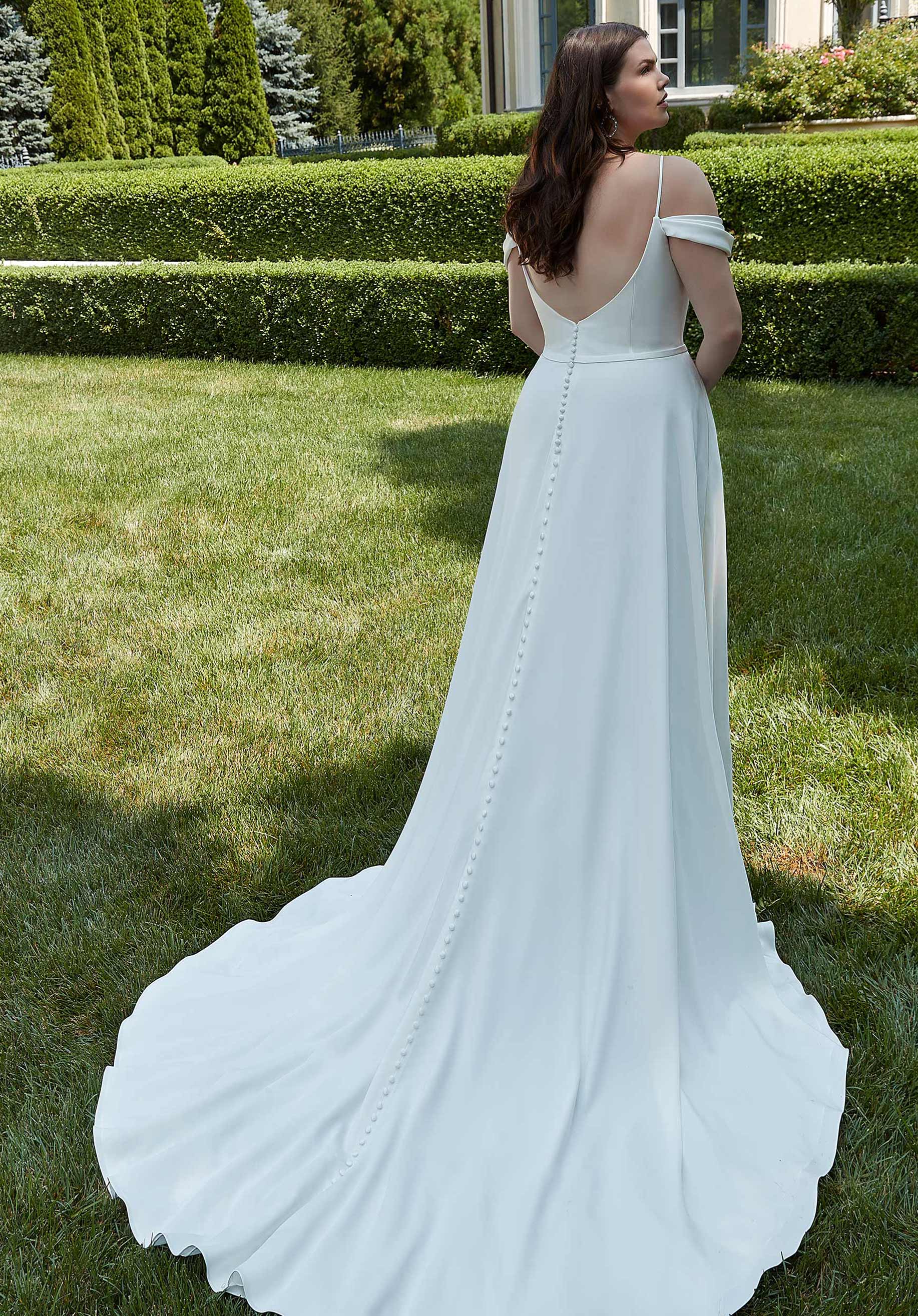 Woman in a white off-shoulder dress standing on grass with a garden background