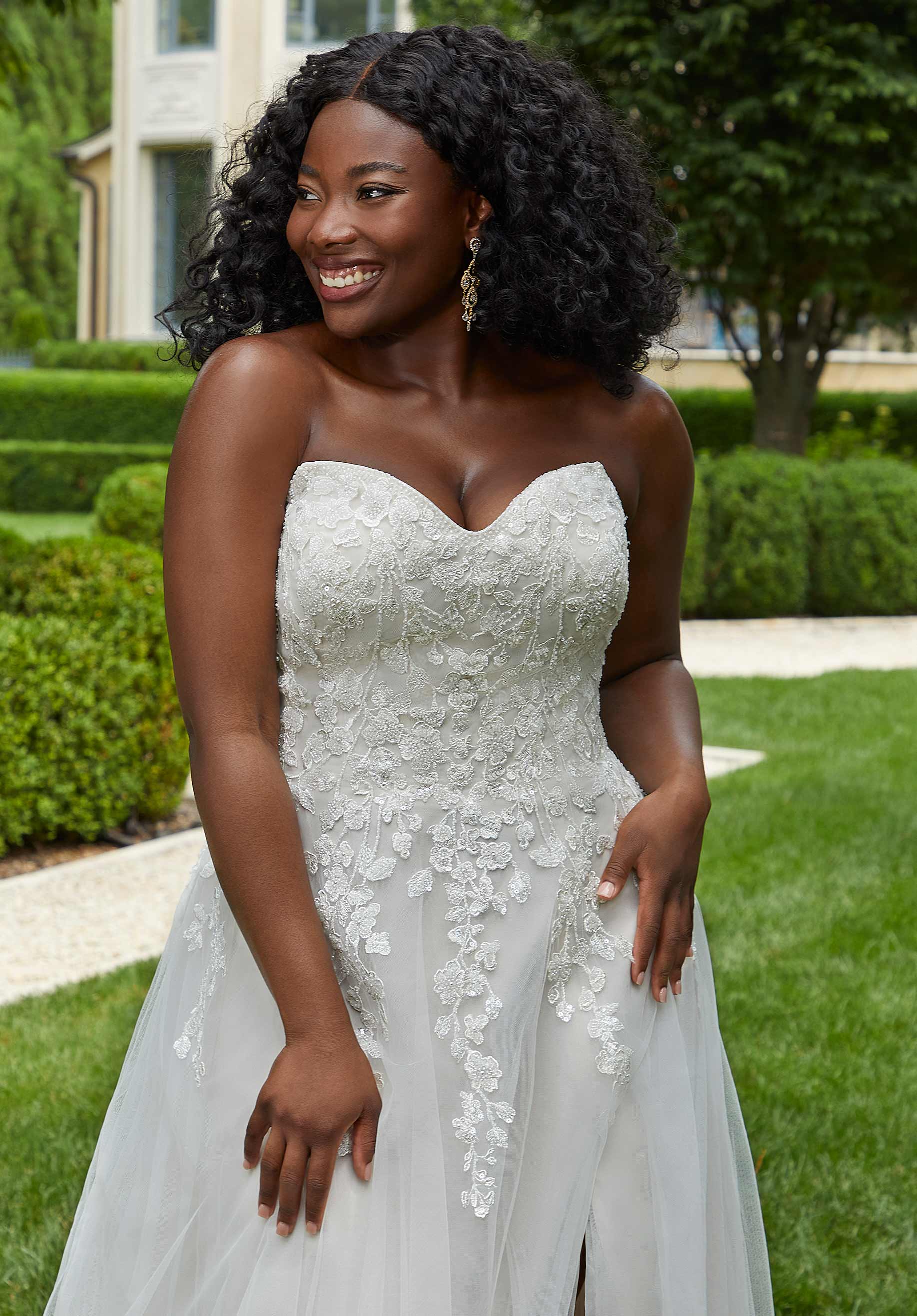 Woman in a white wedding dress standing outdoors with greenery in the background