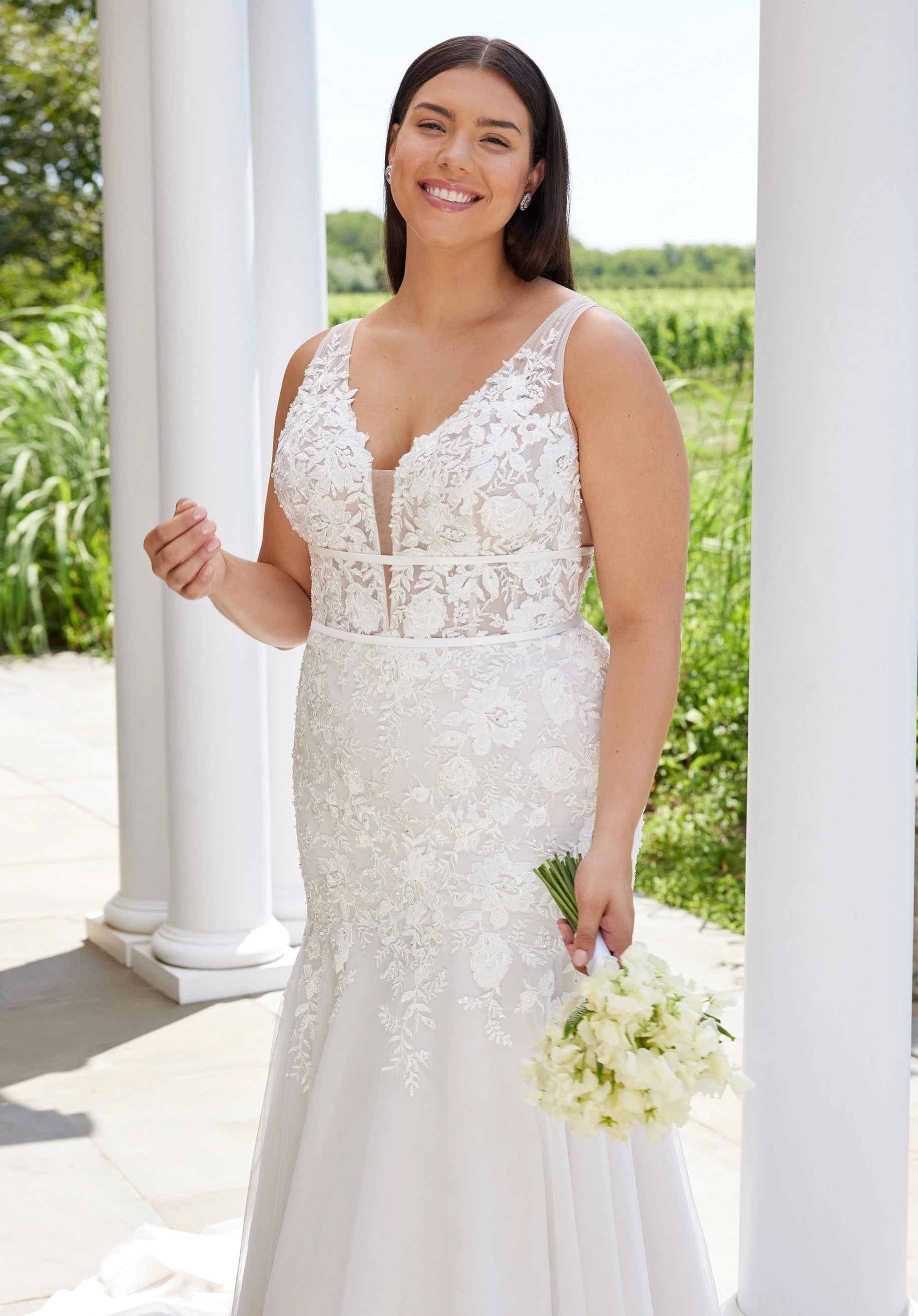 Woman in a white lace wedding dress holding a bouquet outdoors.