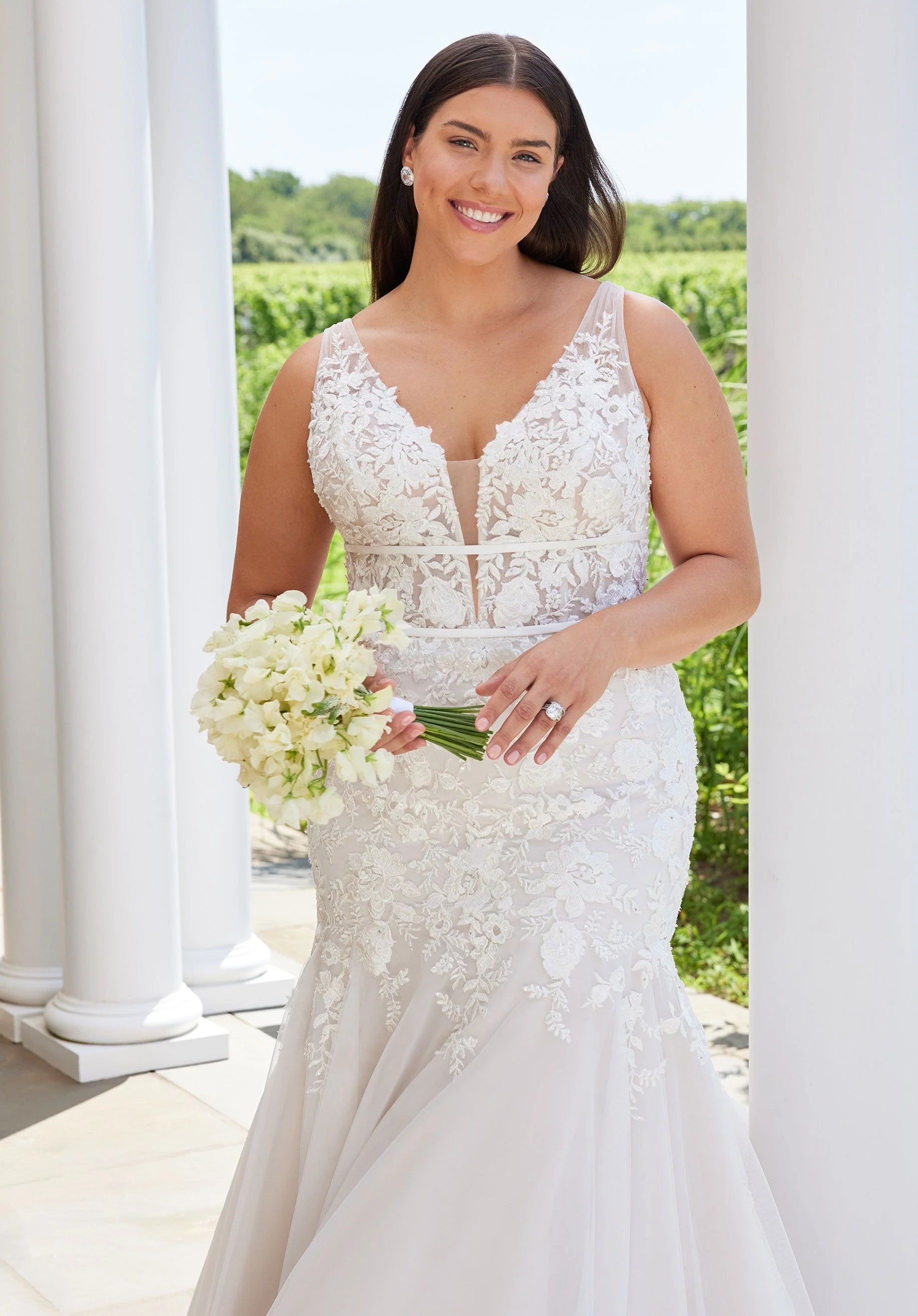 Woman in a white lace wedding dress holding flowers outdoors.