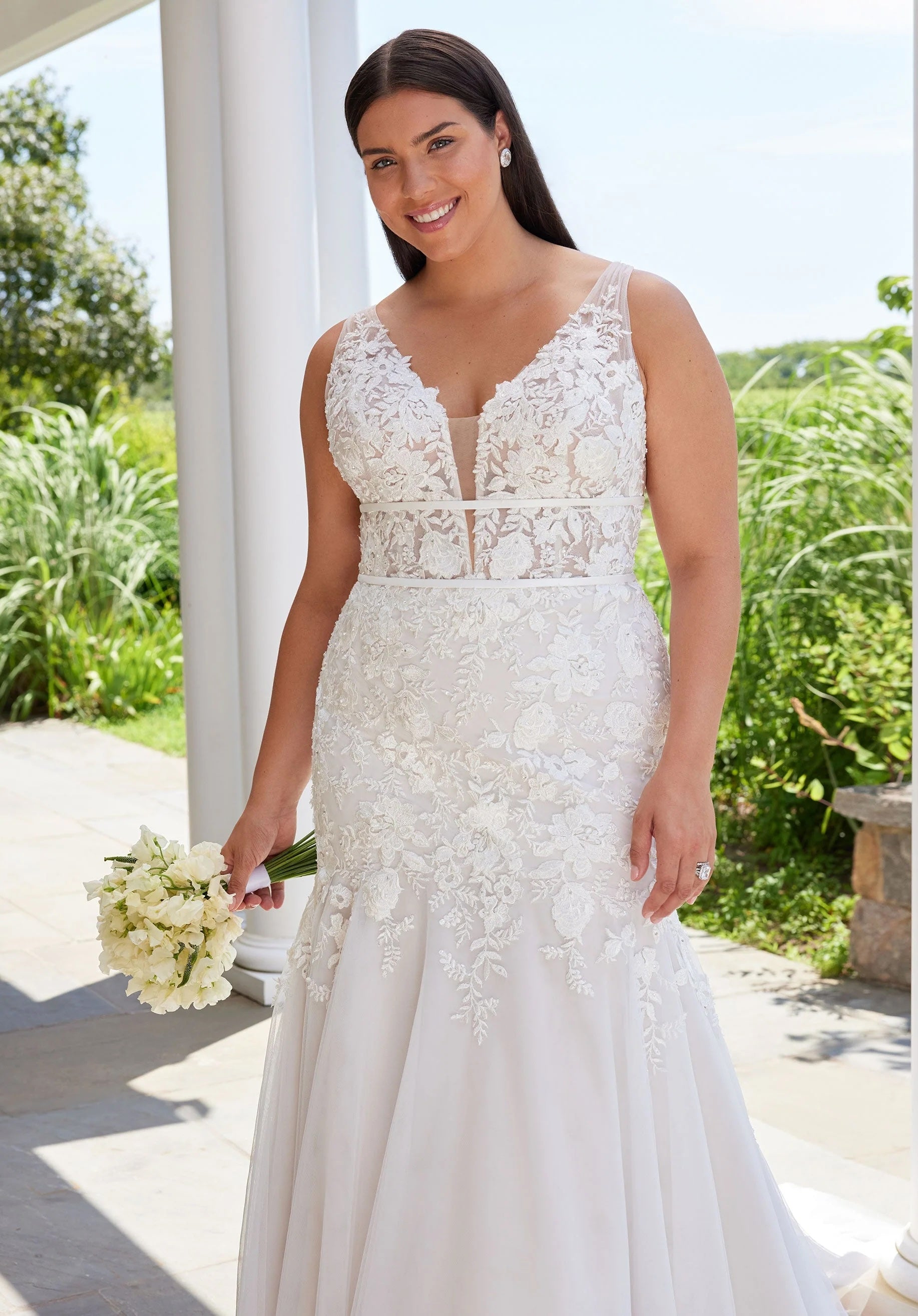 Woman in a white lace wedding dress holding flowers outdoors.